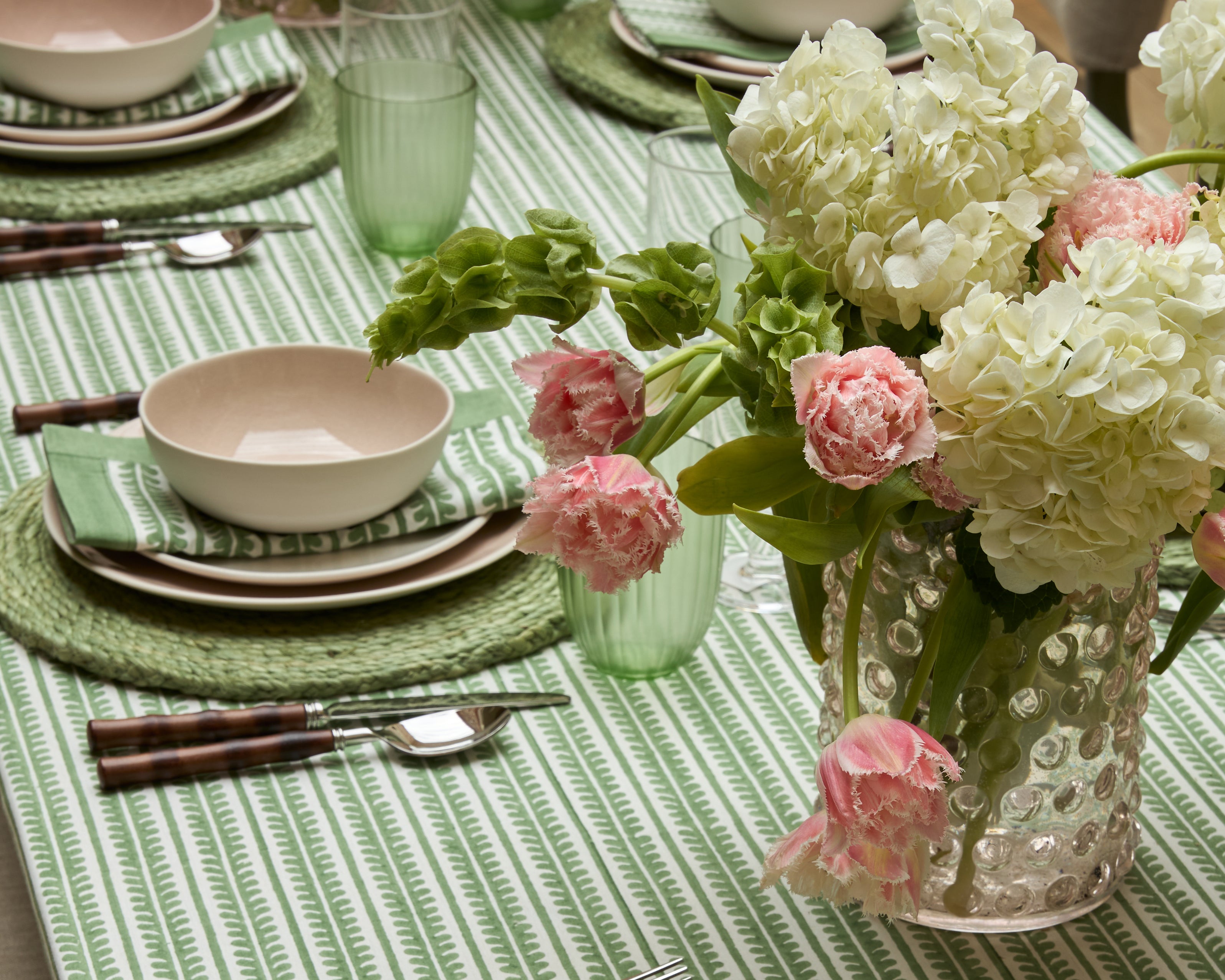 Green and pink dining lifestyle image, featuring the green Bel tablecloth, bel napkins and green Jute placemats