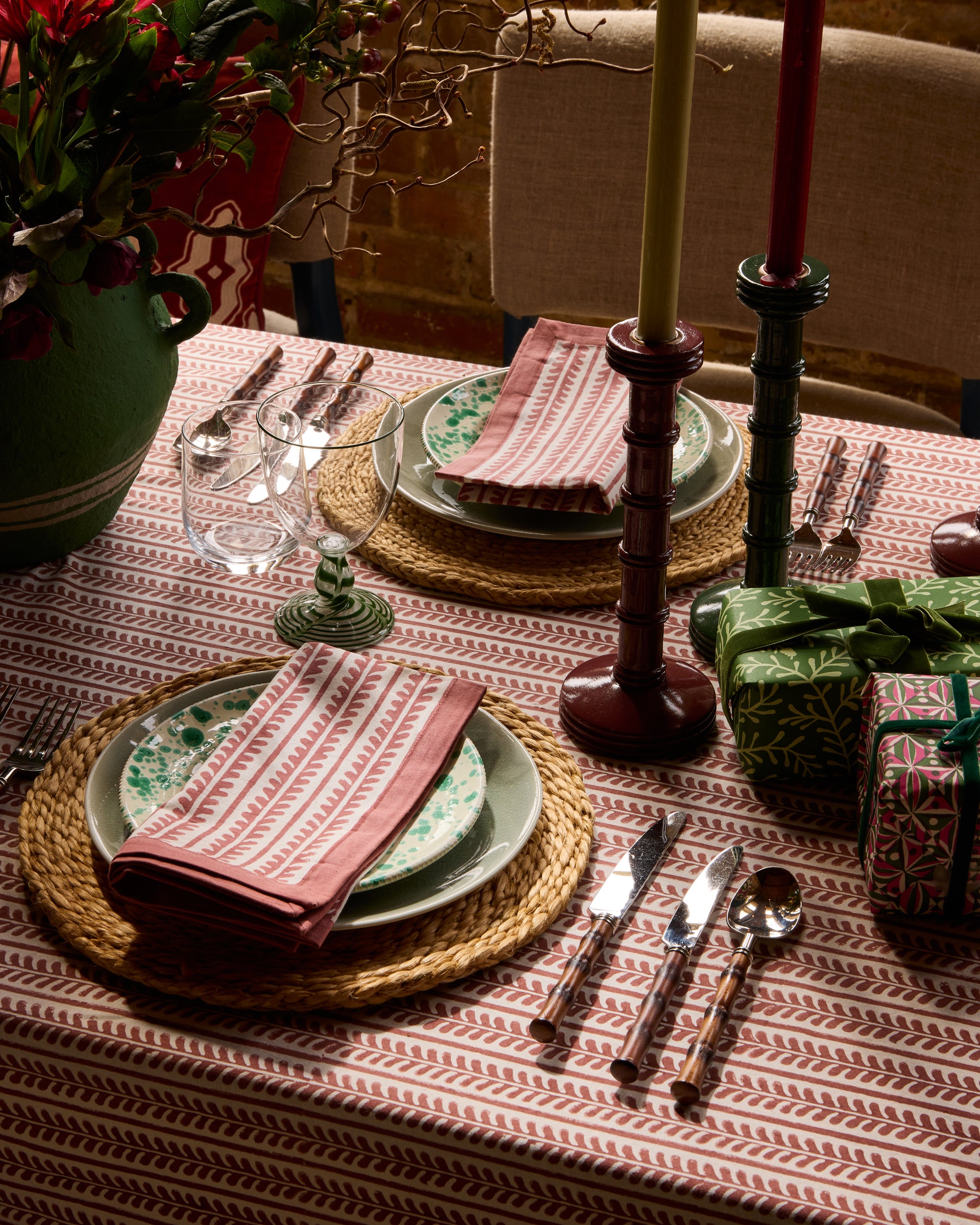 Festive dining set for two, featuring red bel linen napkins and red bel tablecloth. With red and green column candlesticks and presents