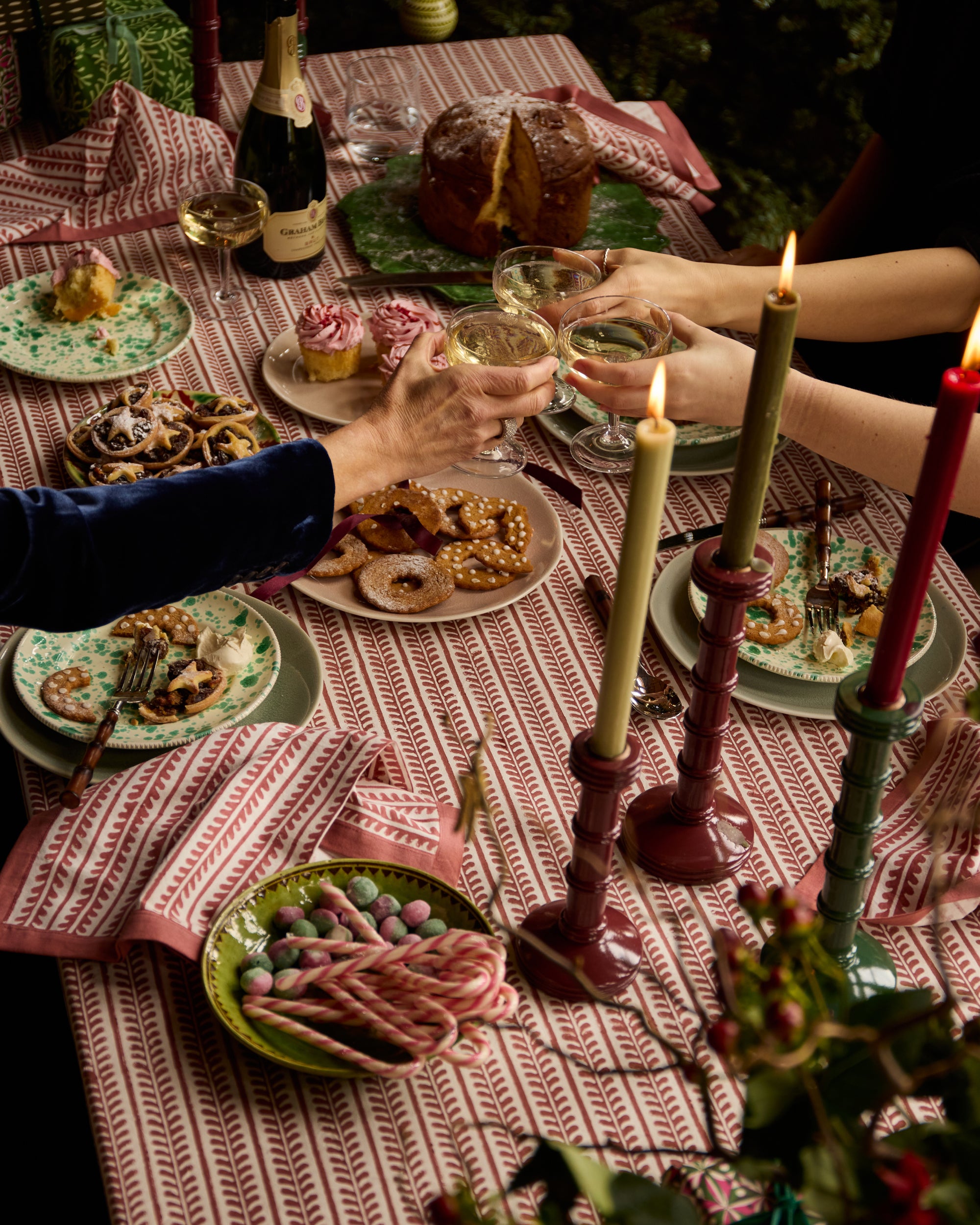 Red and green festive Christmas dining table, with red bel table linens and column candlesticks