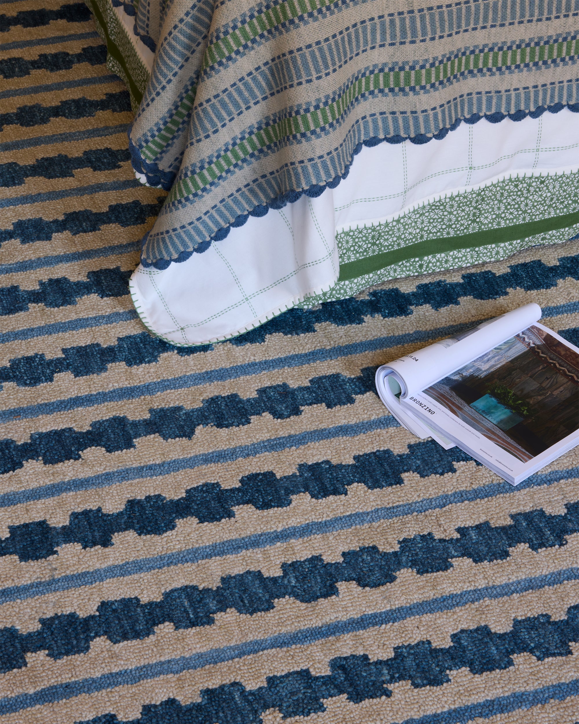 Textured rug with blue and beige pattern, partially covered by a striped blanket.