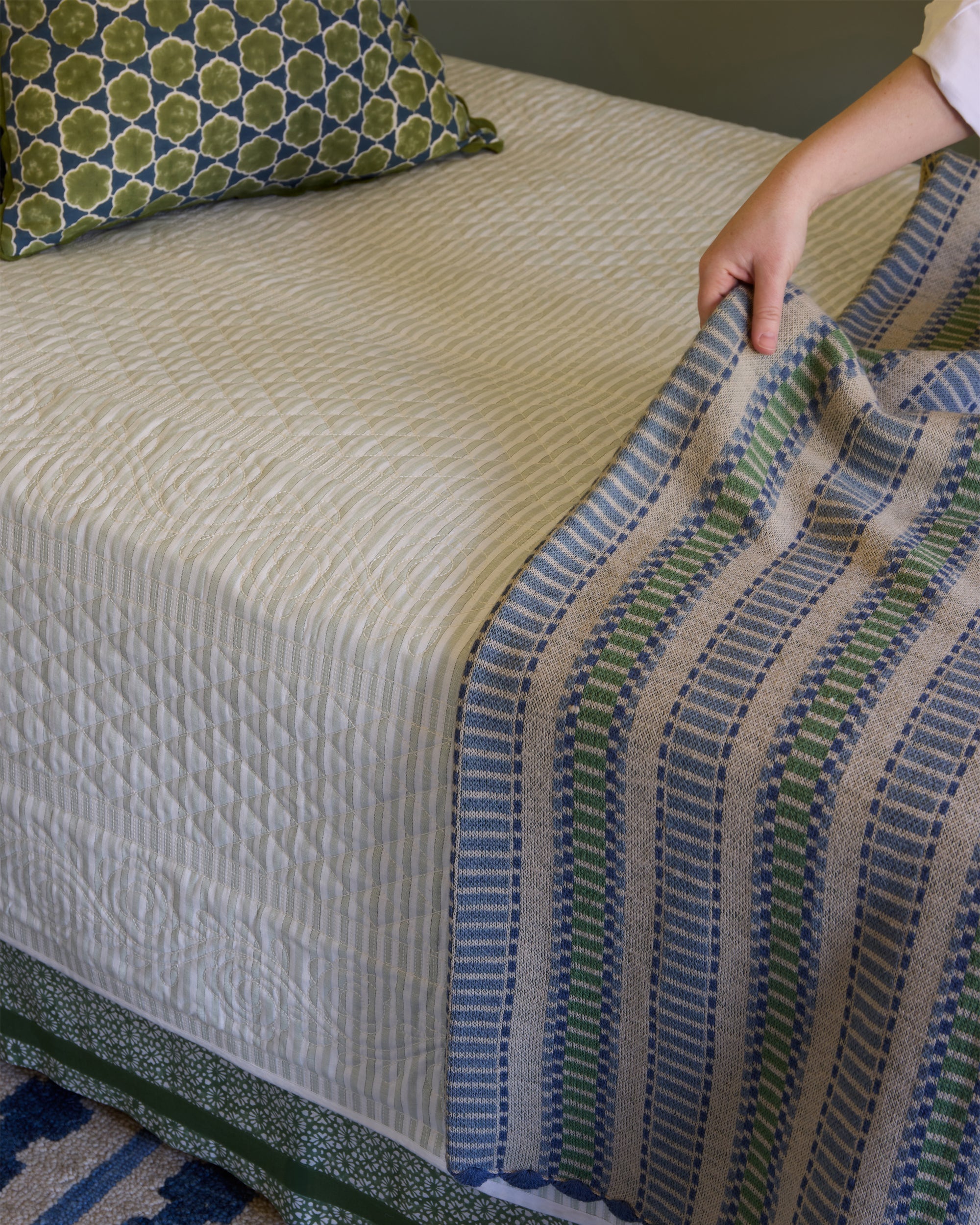 Textured throw with geometric pattern on a bed, being adjusted by a hand.