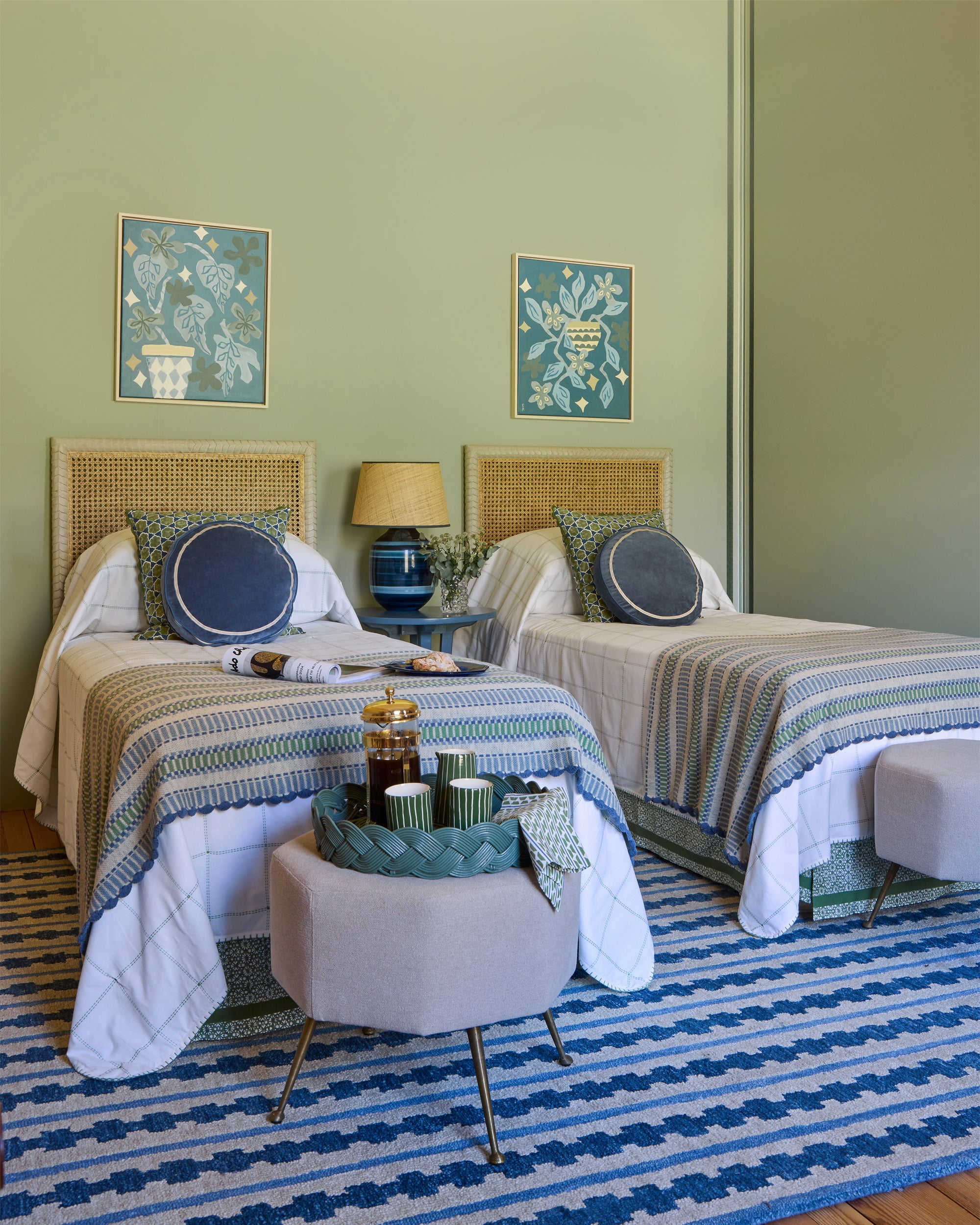 Two twin beds in a room with decorative cushions, lamps, and artwork on a green wall.
