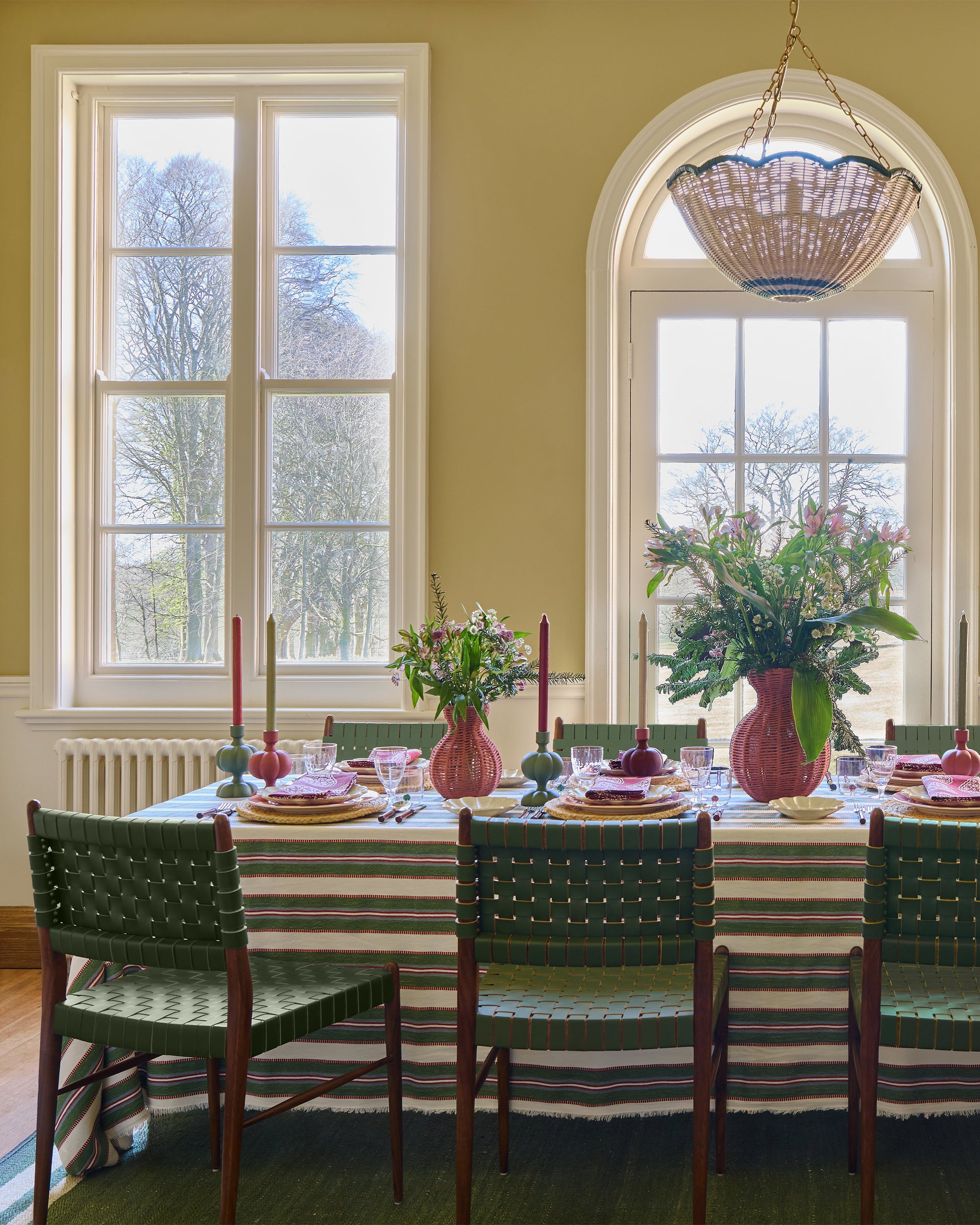 Dining room with a table set for dinner, green chairs, and floral arrangements.