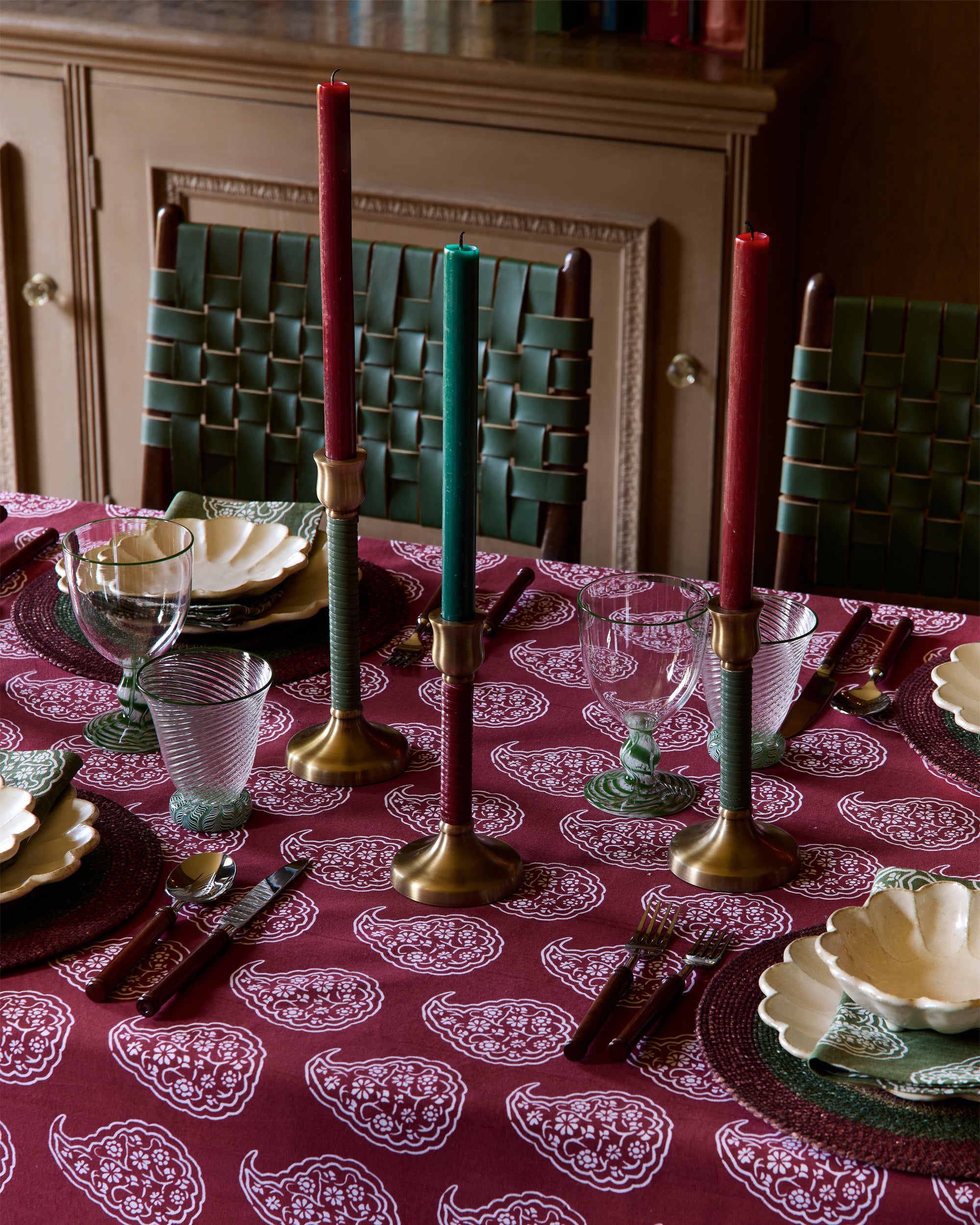 Dining table set with red and green candles on a patterned tablecloth.