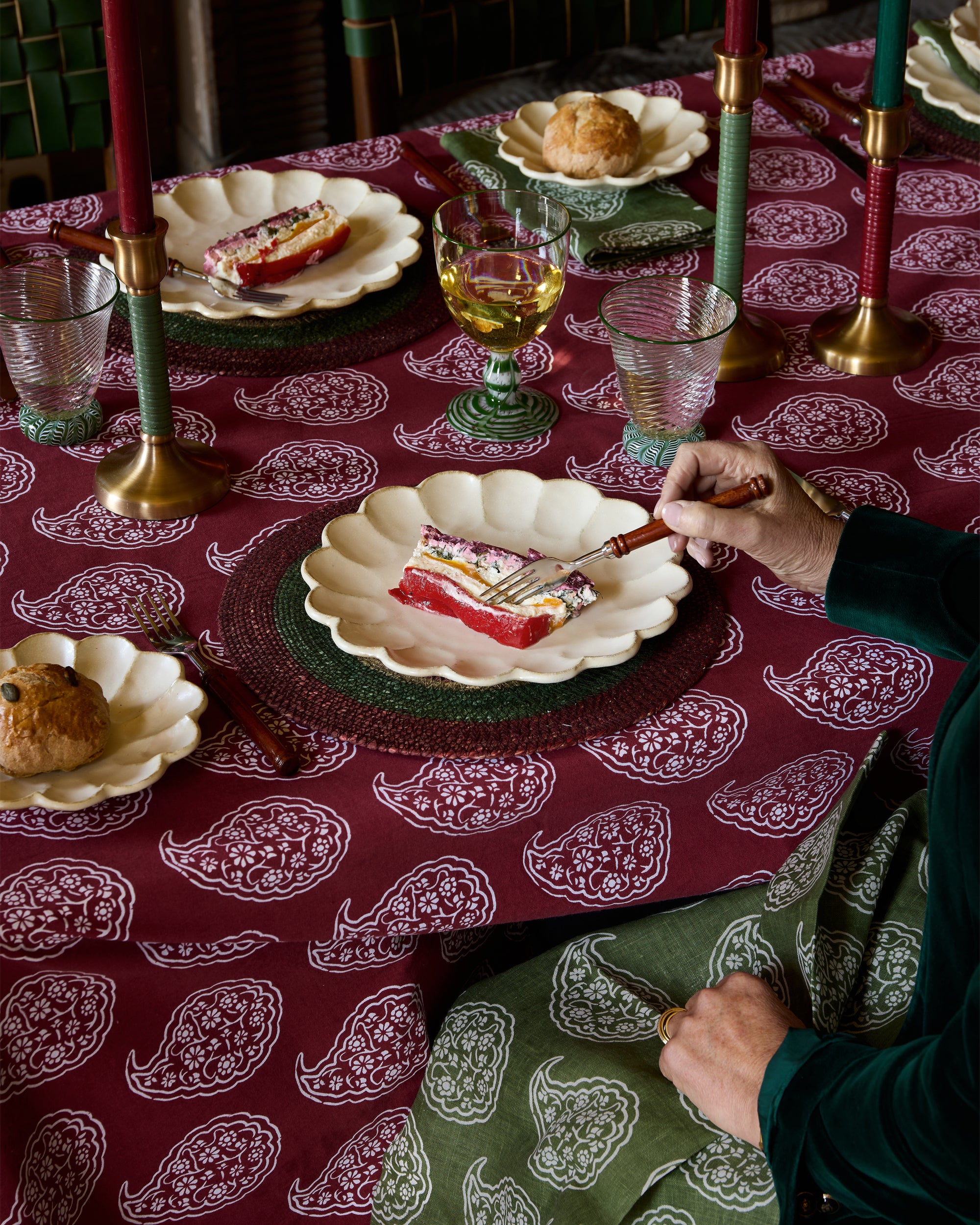 Dining table with a red paisley tablecloth, plates with food, and a person sitting at the table.