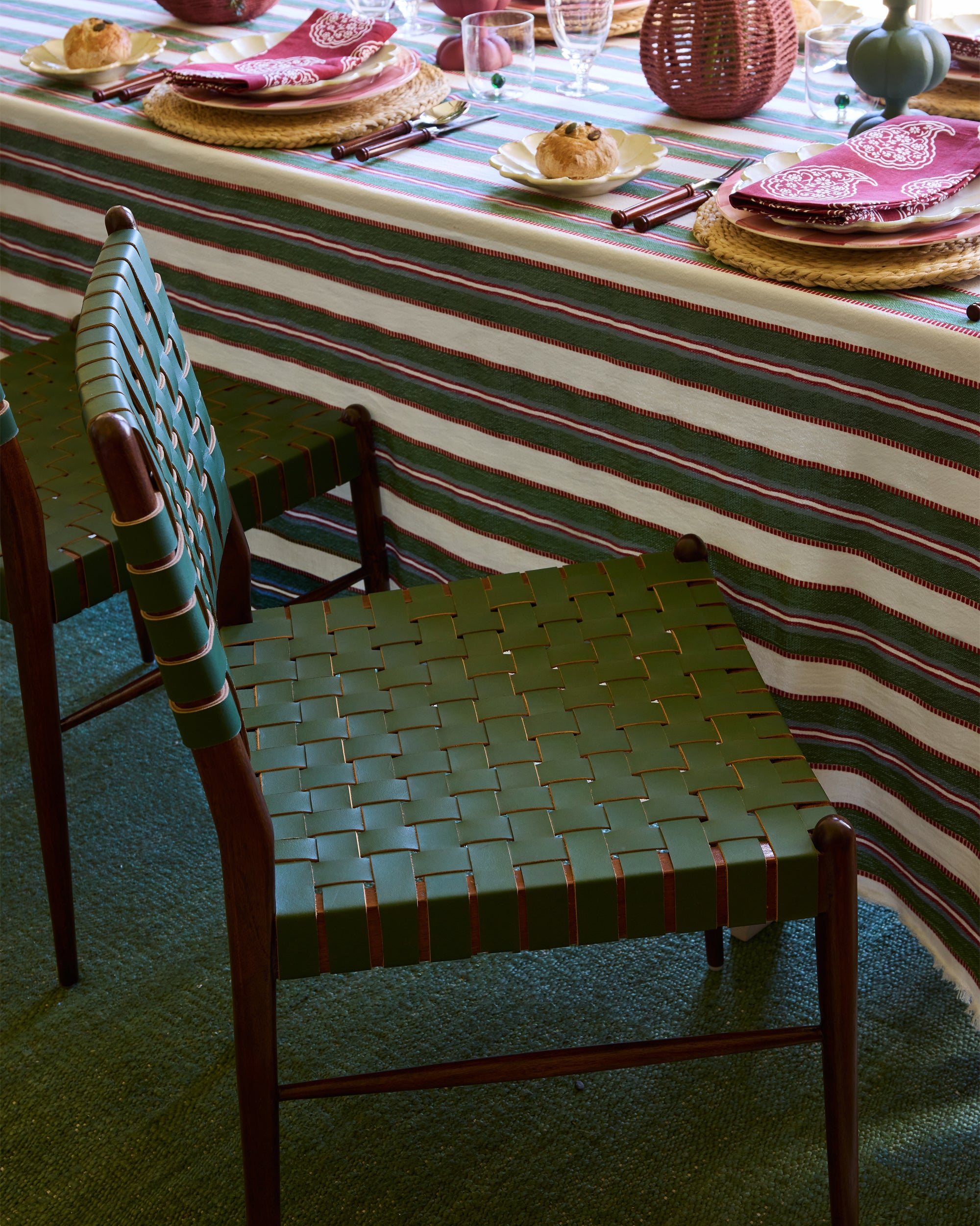 Green woven chair in front of a table with striped tablecloth and place settings.