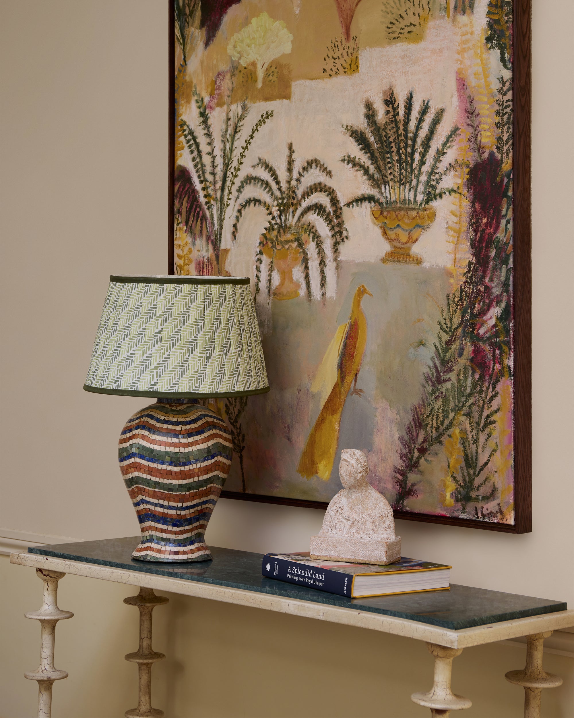 Decorative table with a lamp, books, and a statue against a wall with a colorful abstract painting.