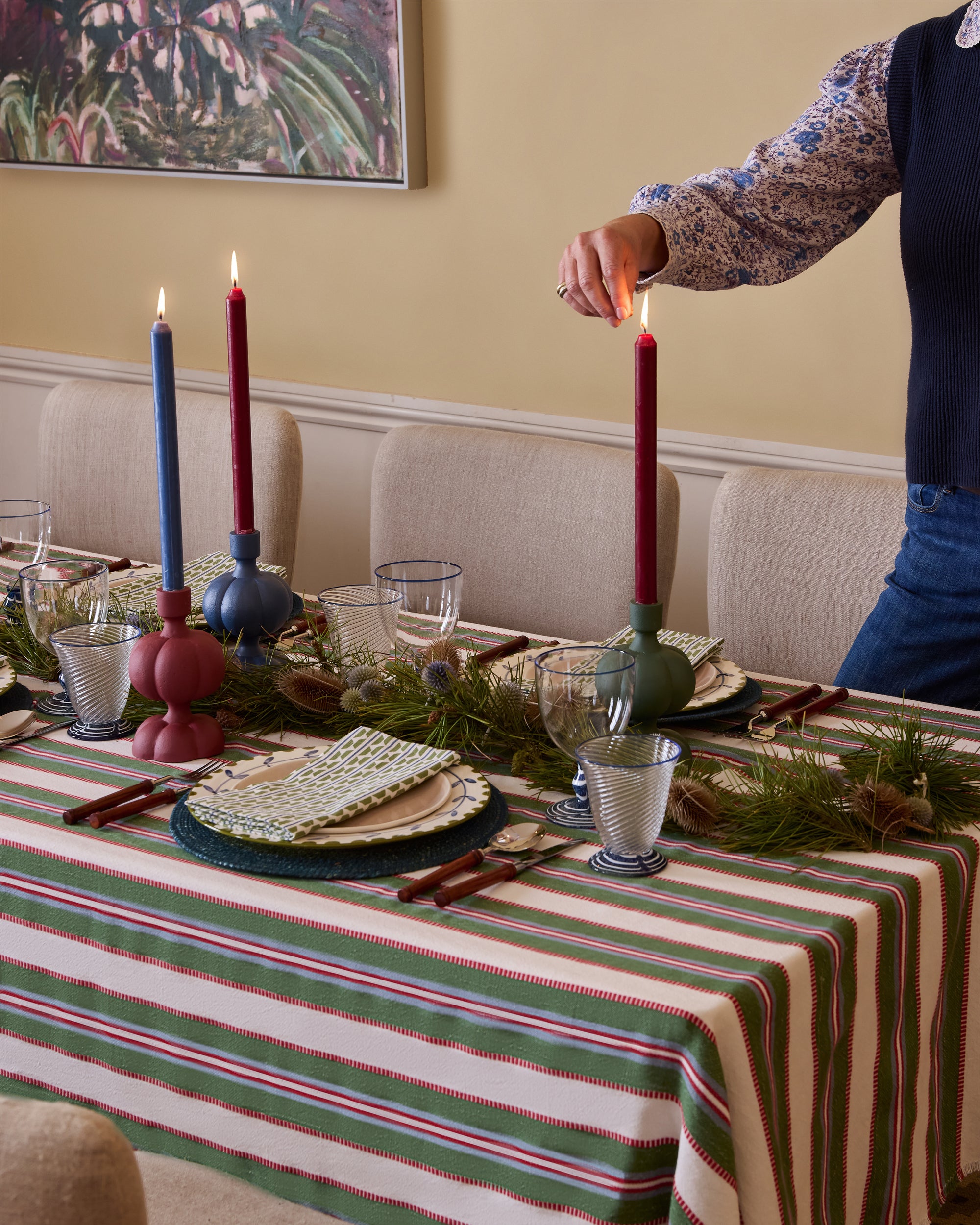 Person lighting a candle on a decorated table with a striped tablecloth