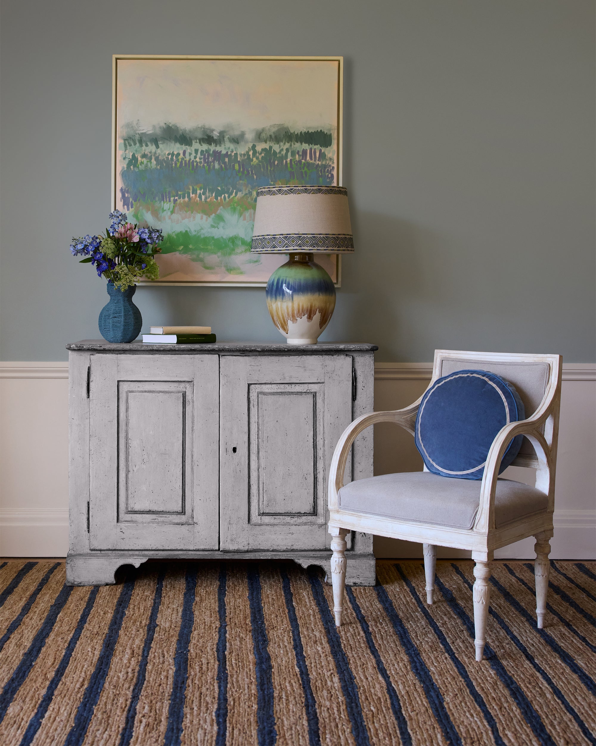 Room interior with a vintage cabinet, chair, and decorative items against a gray wall.