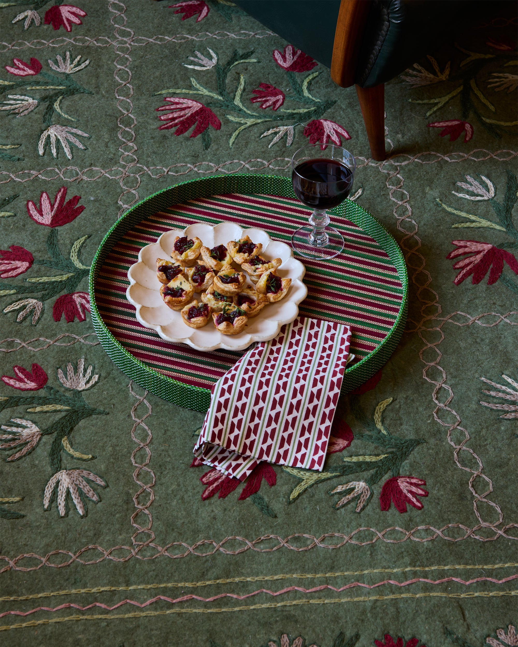 Tray with cookies and a glass of red wine on a decorative green tablecloth with floral patterns.