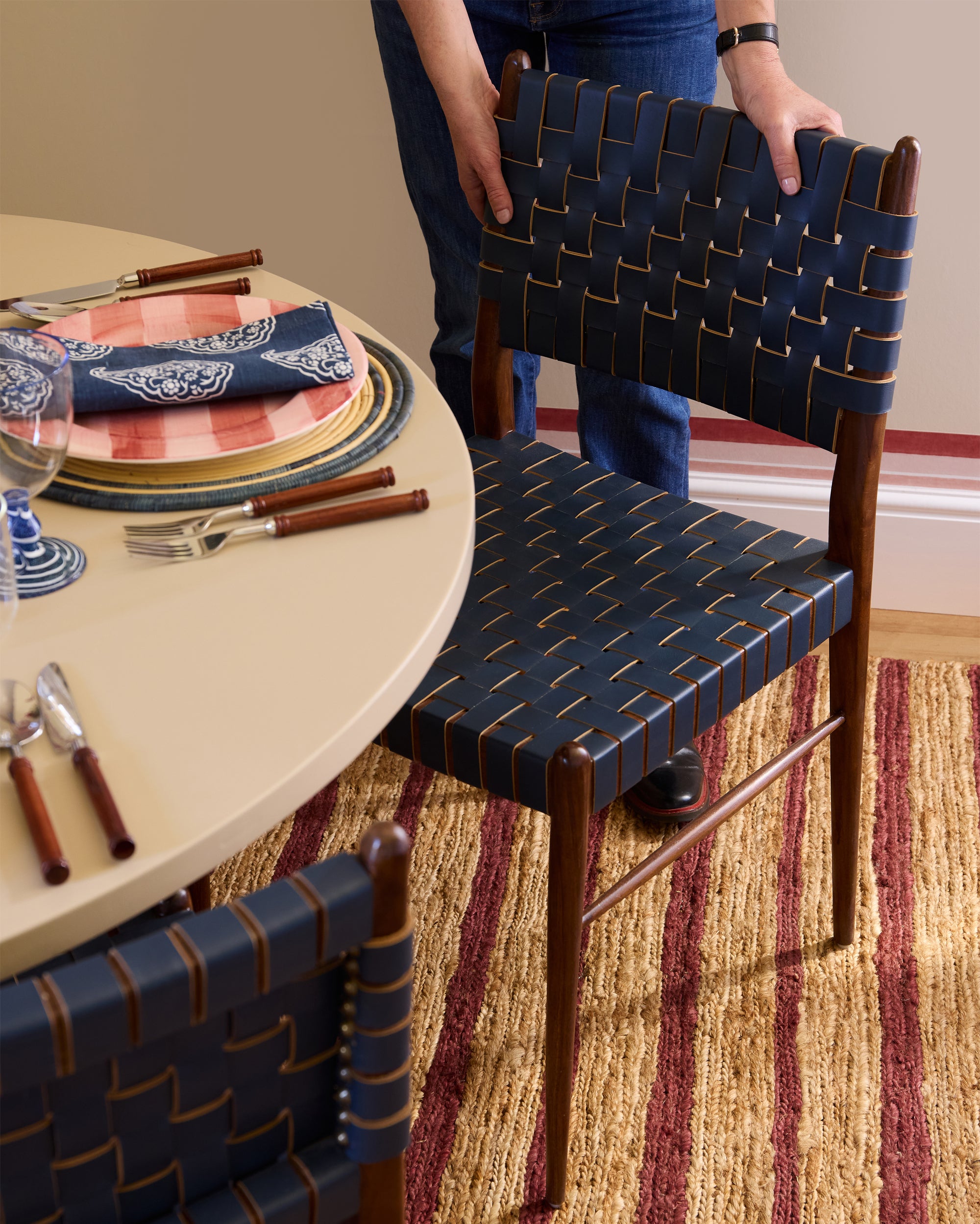 Person holding a woven chair next to a dining table with place settings.