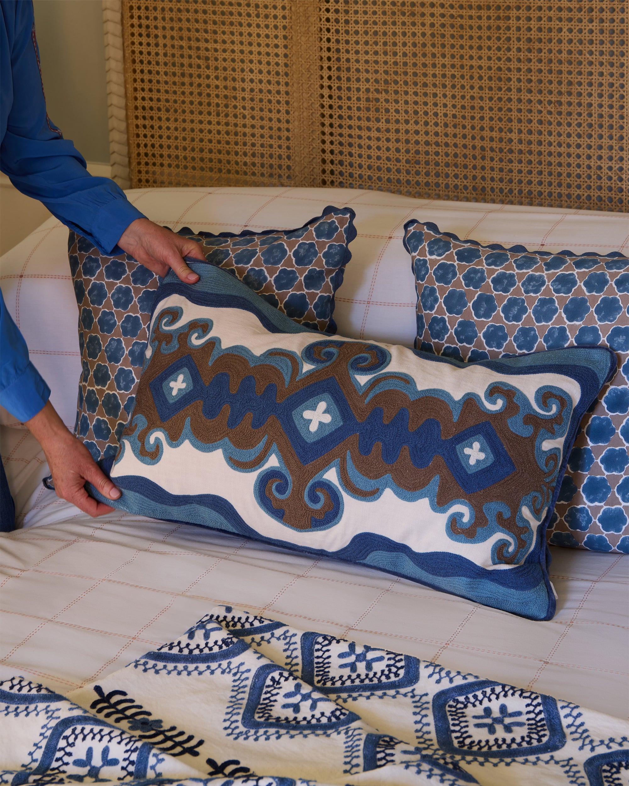 Person arranging decorative pillows with geometric patterns on a bed.