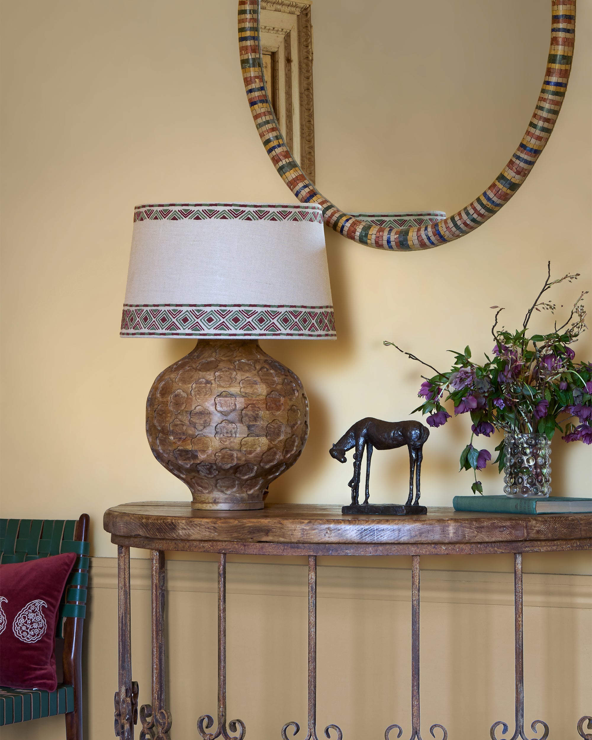Decorative lamp on a wooden console table with a horse figurine and flowers against a beige wall.