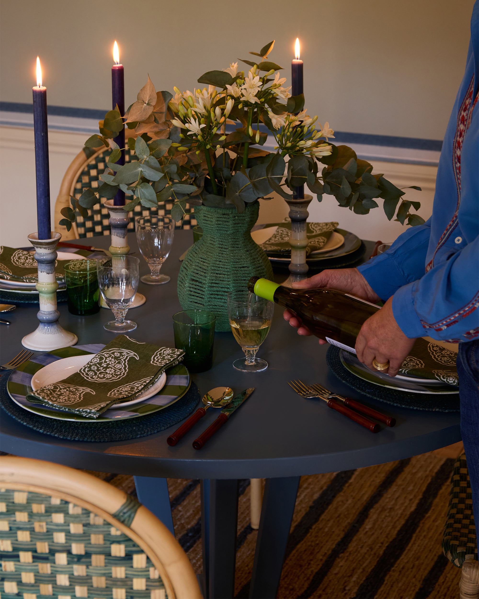 Person pouring wine at a decorated dining table with candles and flowers.