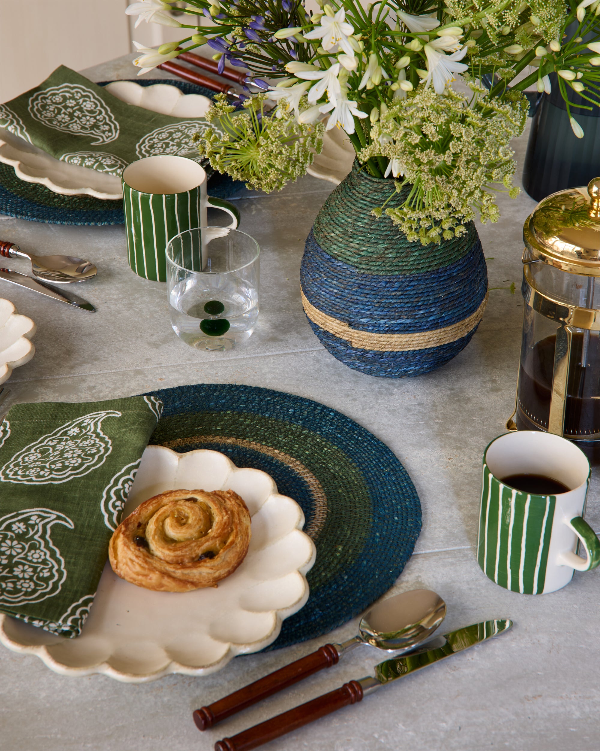 Table setting with green and white tableware, flowers, and a pastry.