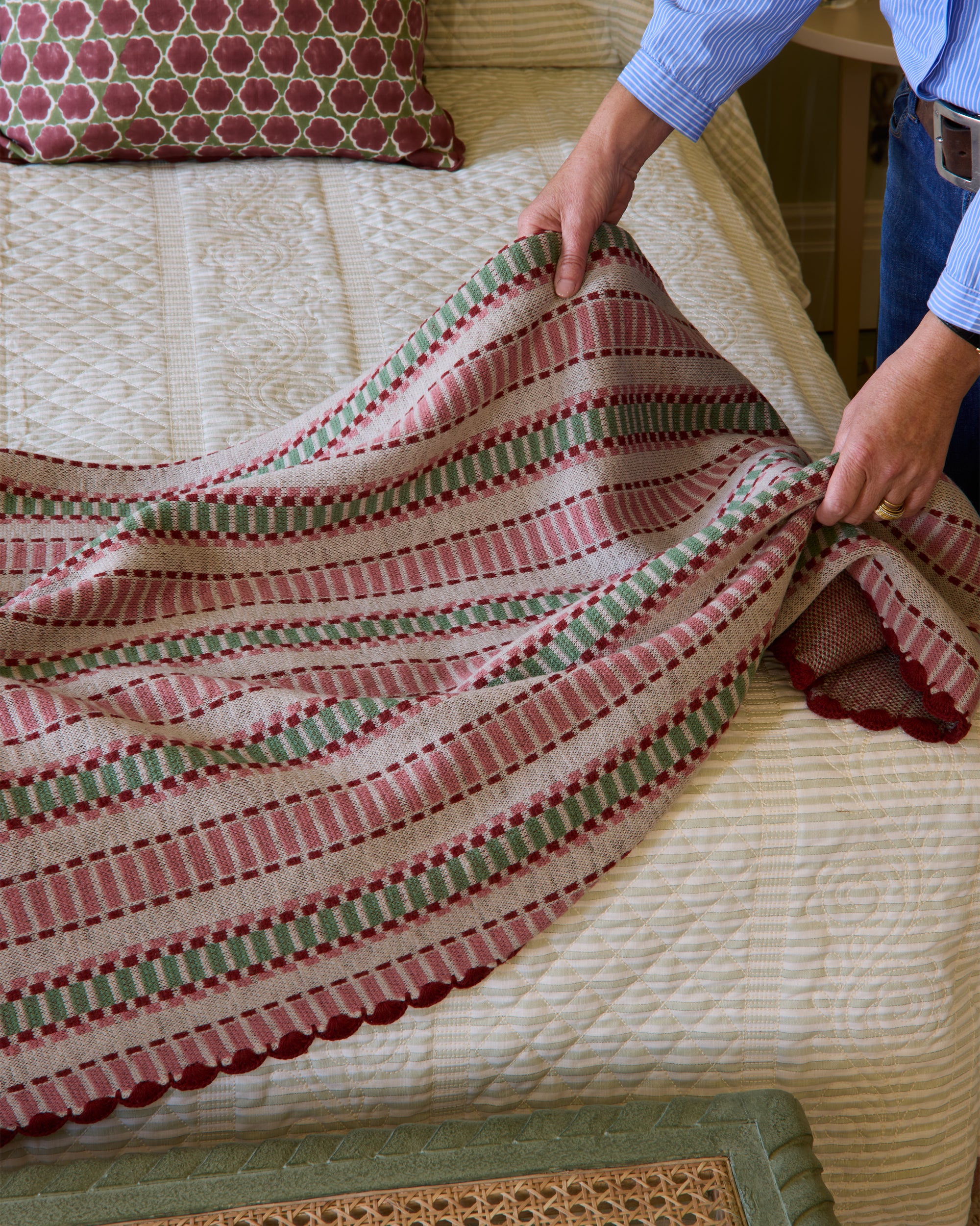 Person arranging a striped throw on a bed