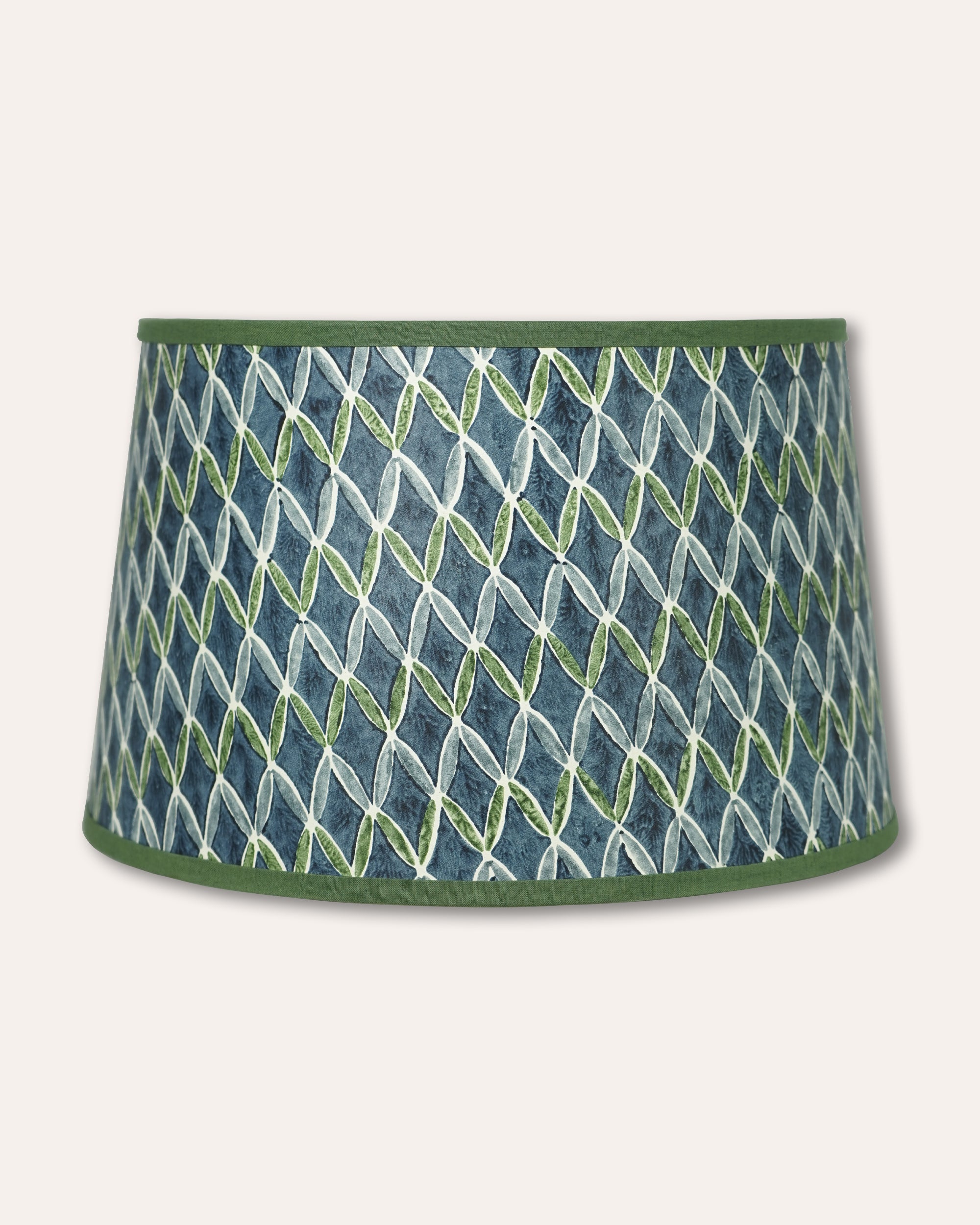 A tapered drum lampshade featuring a blue and green geometric pattern with a solid green top and bottom trim, shown against a light beige background.