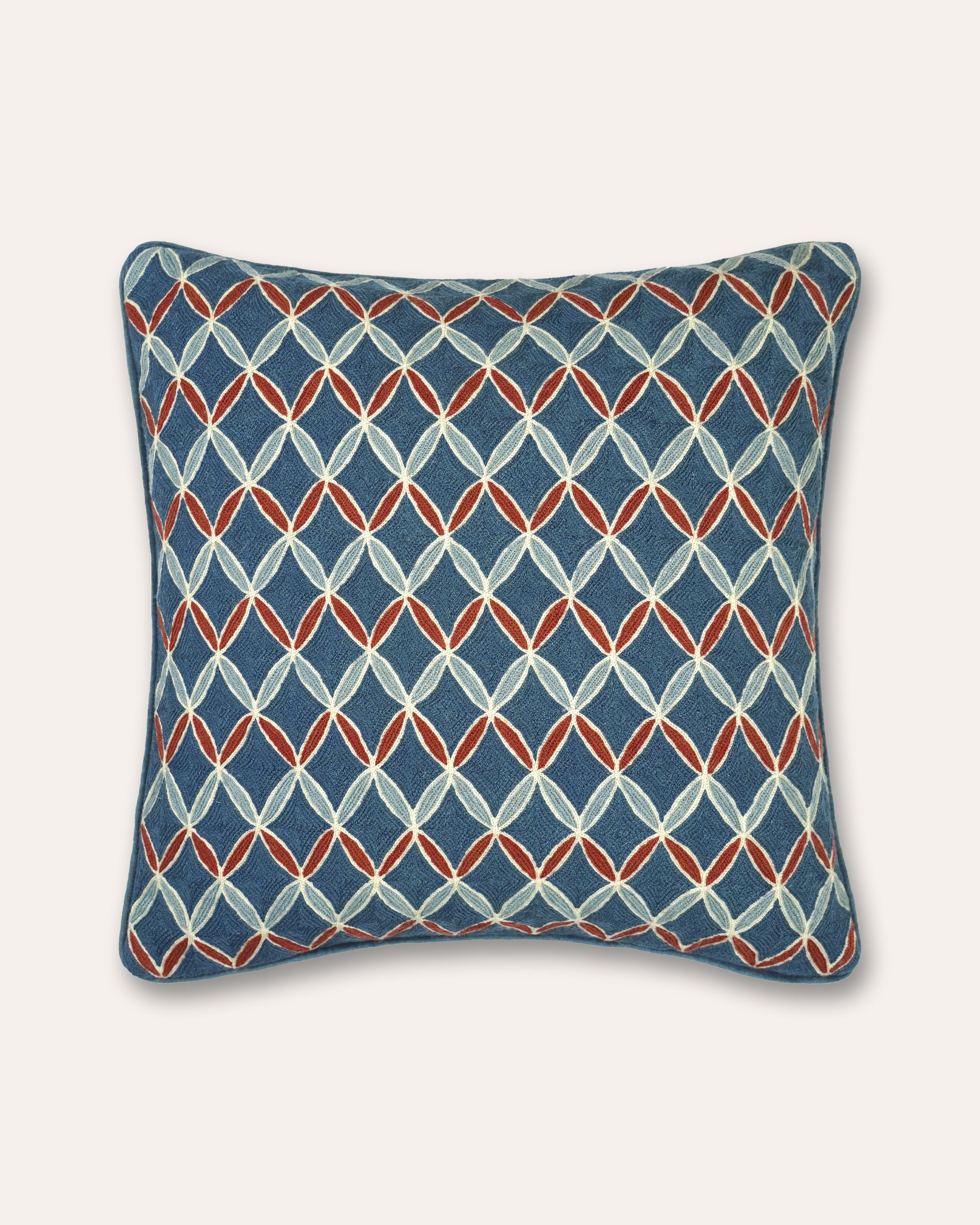 A square decorative cushion featuring a geometric interlocking diamond pattern in blue, light grey, and rust orange on a solid off-white background.