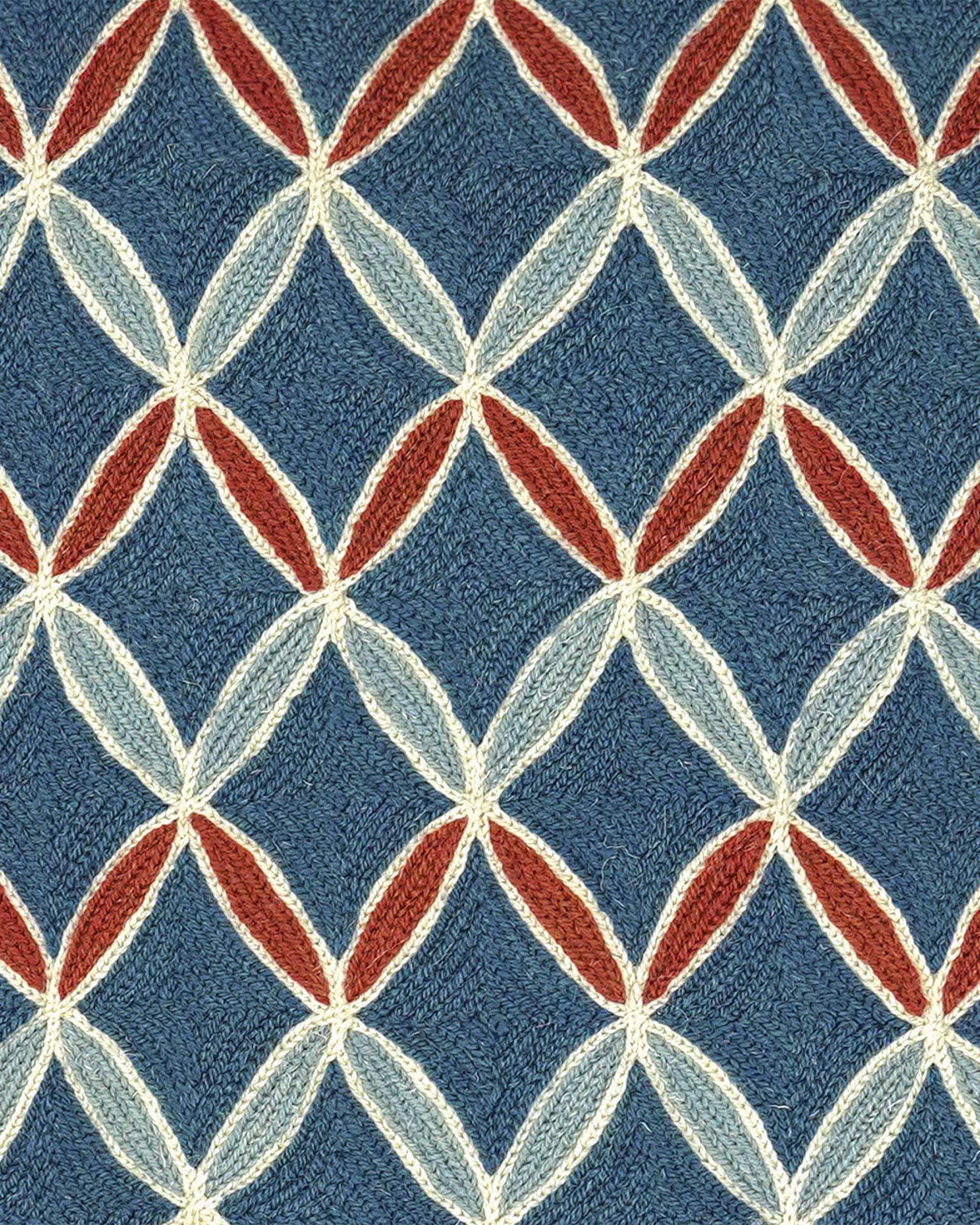 A close-up of a woven fabric pattern featuring a repeating geometric diamond design in slate blue, cream, light blue, and rust red.