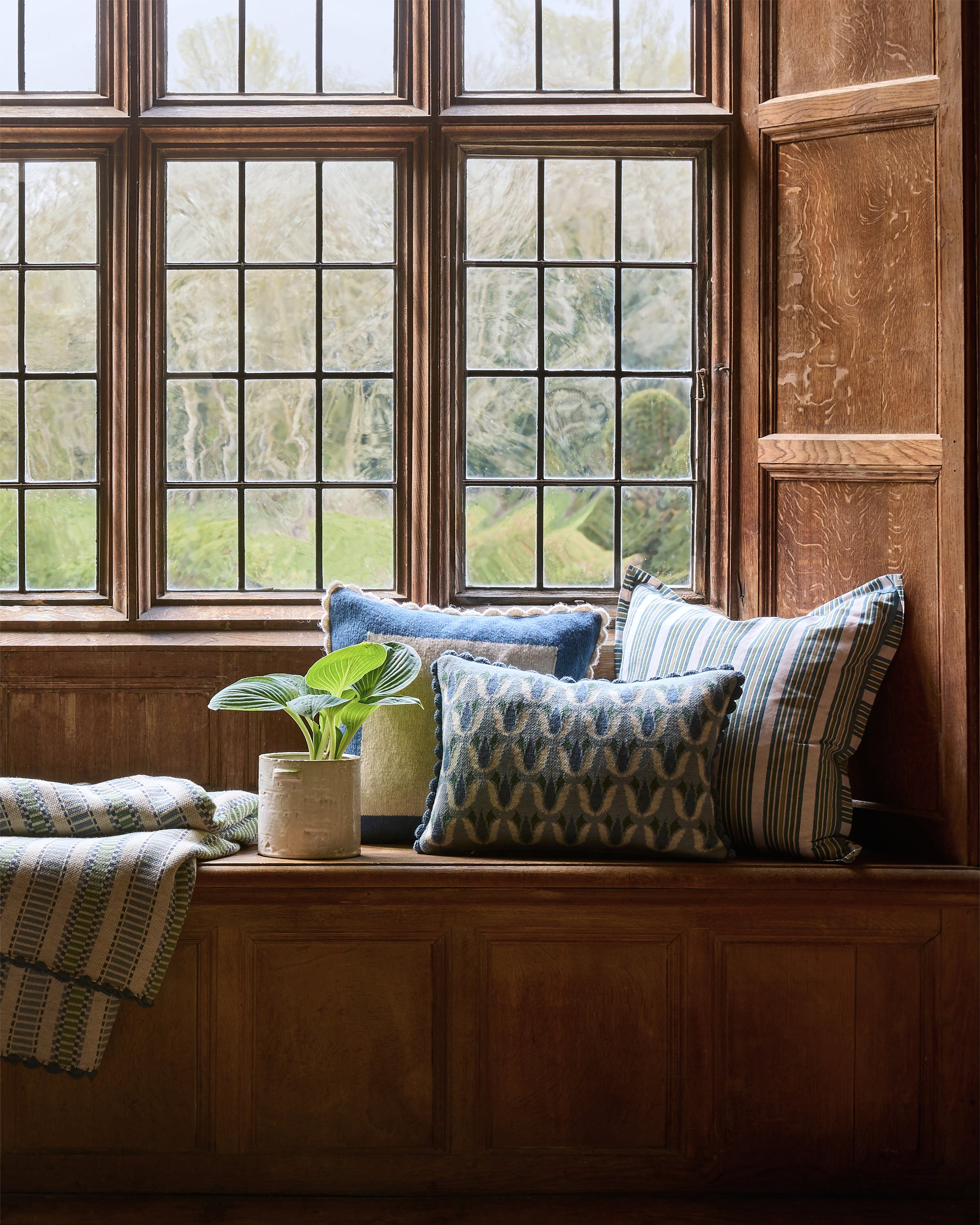 Decorative window seat with cushions and a plant in a room with large windows.