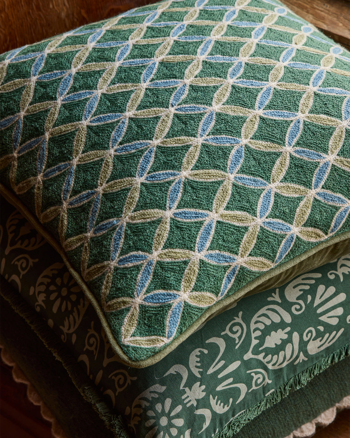 Close up detail of the Aswan trellis embroidered cushion with intricate designs on a wooden surface