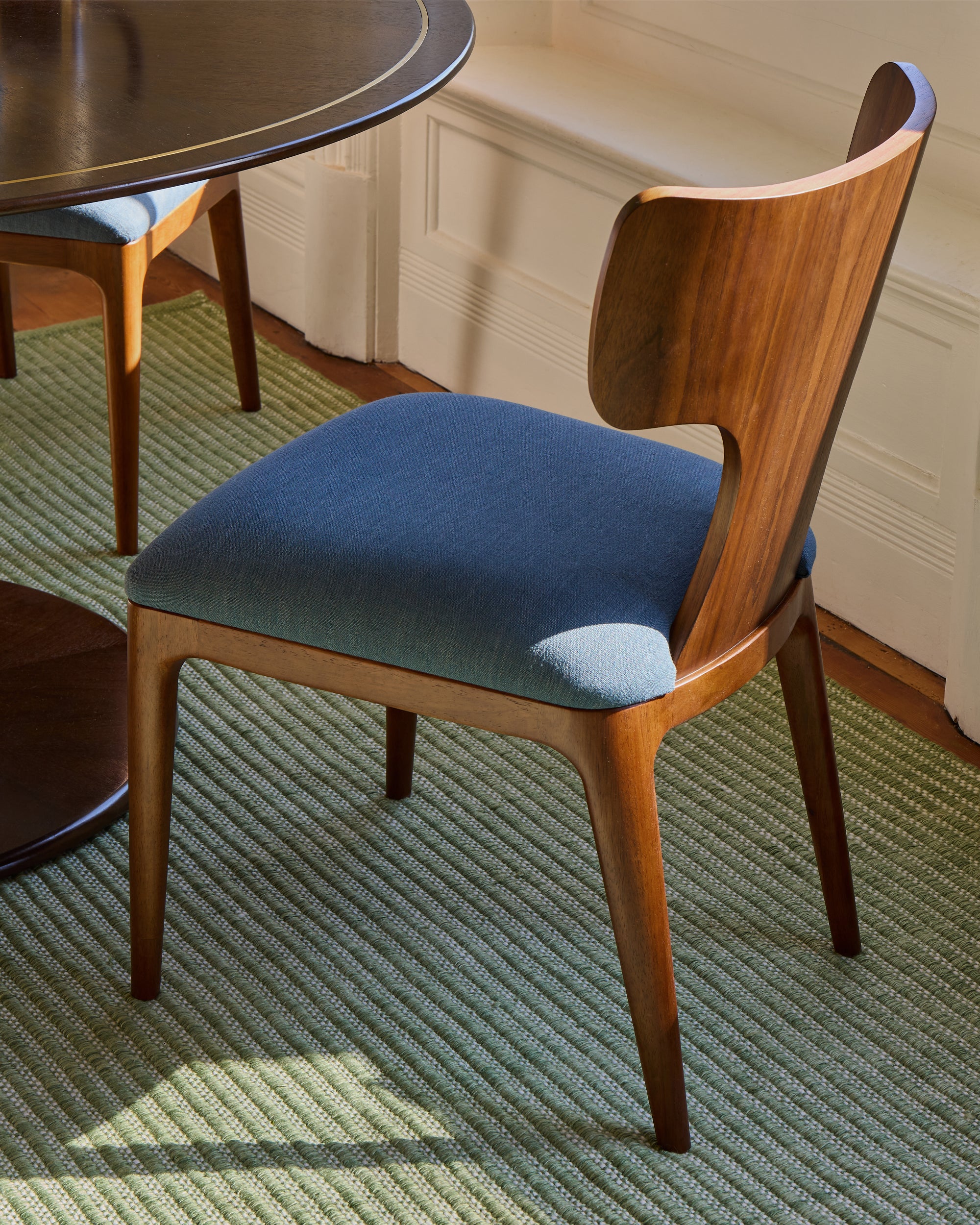 Wooden chair with blue cushion on a green rug.