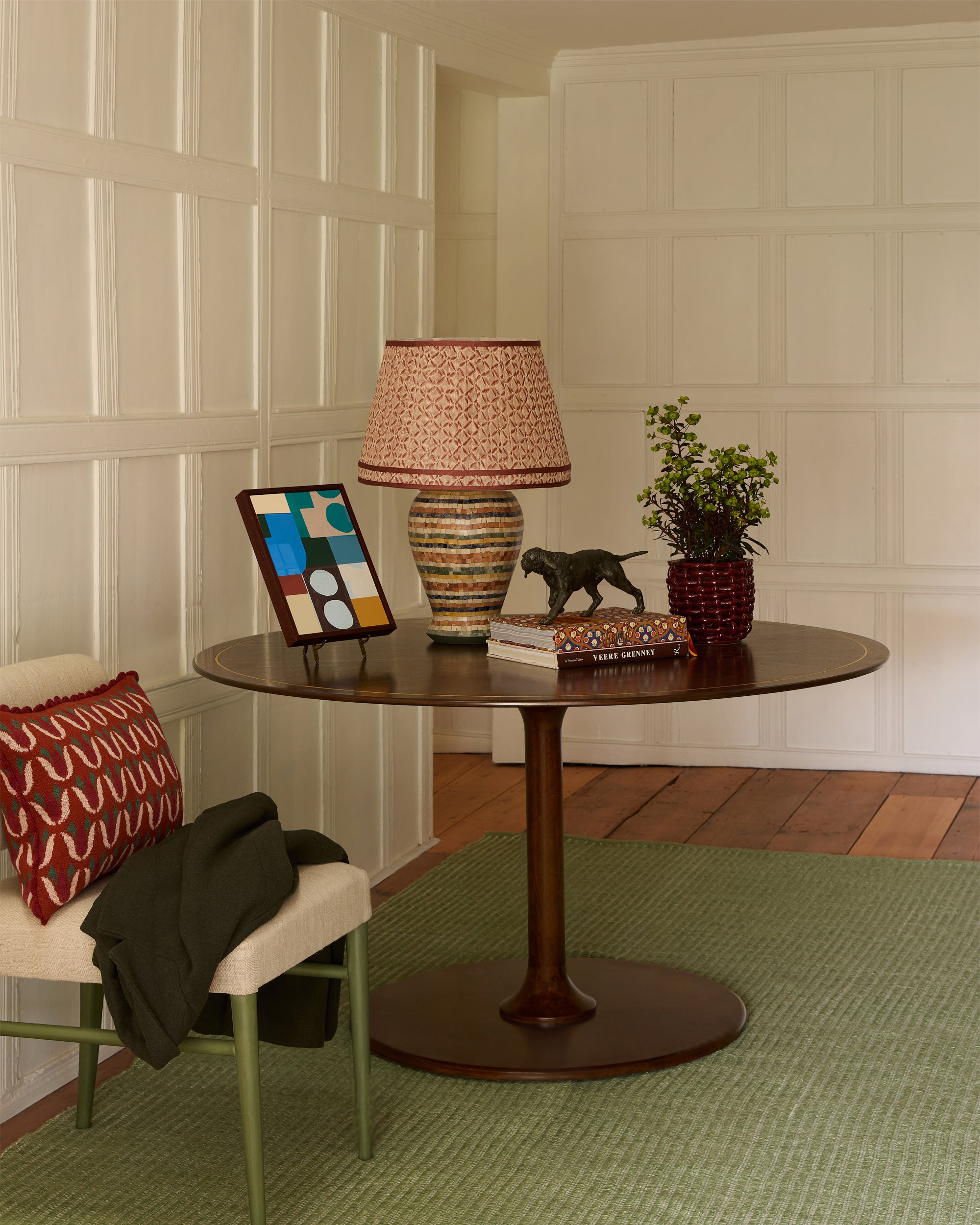 Round wooden table with decorative items in a room with paneled walls and a green rug.