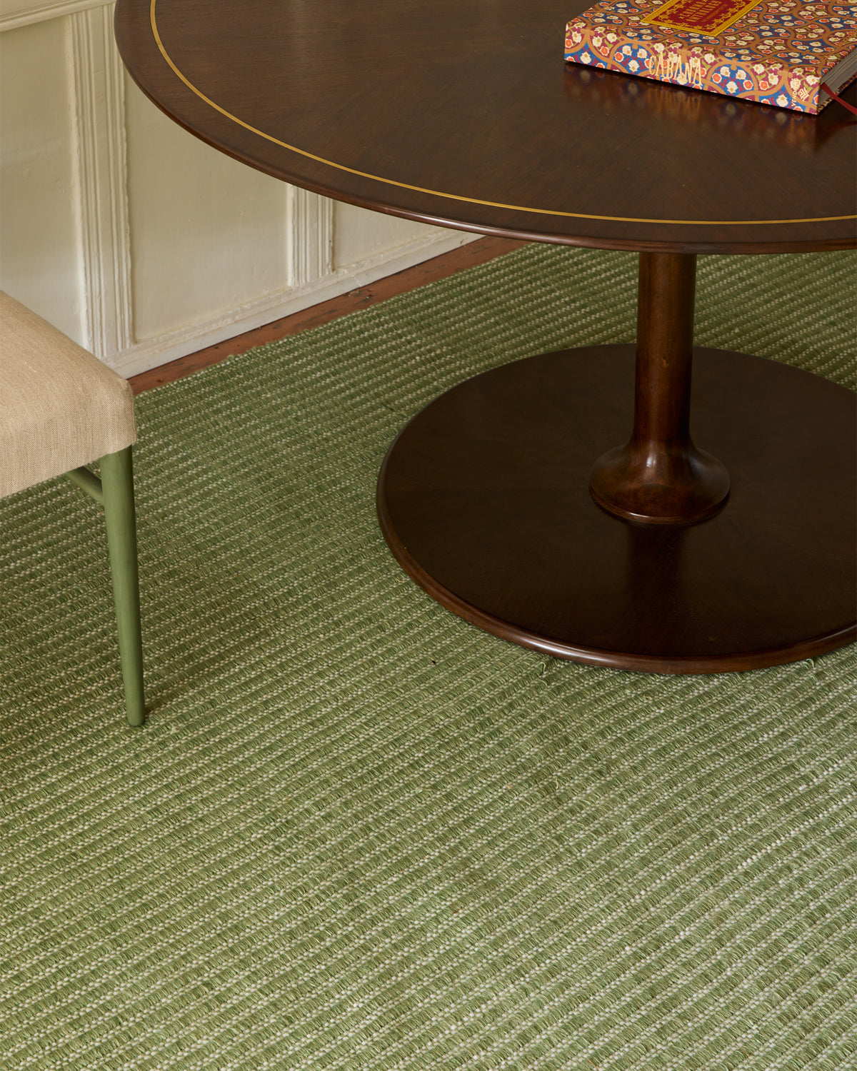 Green striped rug with a wooden table and chair in the background