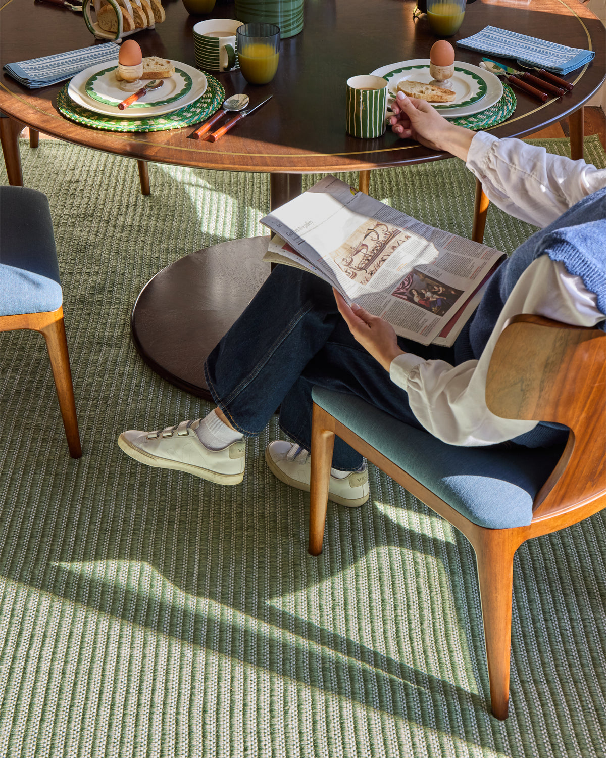 Person reading a book in a cozy room with a table and chairs.