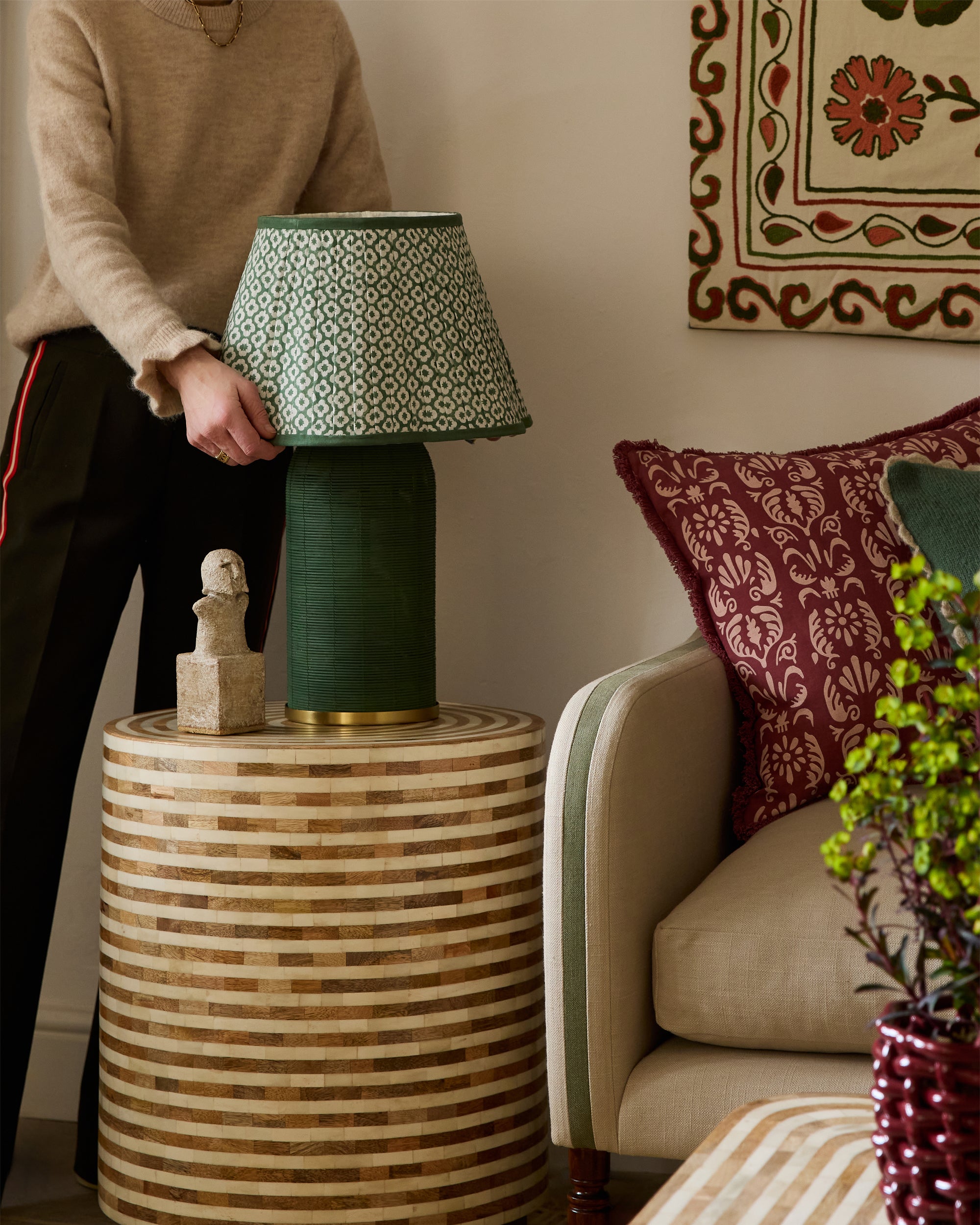 Person holding a green lamp with a patterned shade in a living room setting.