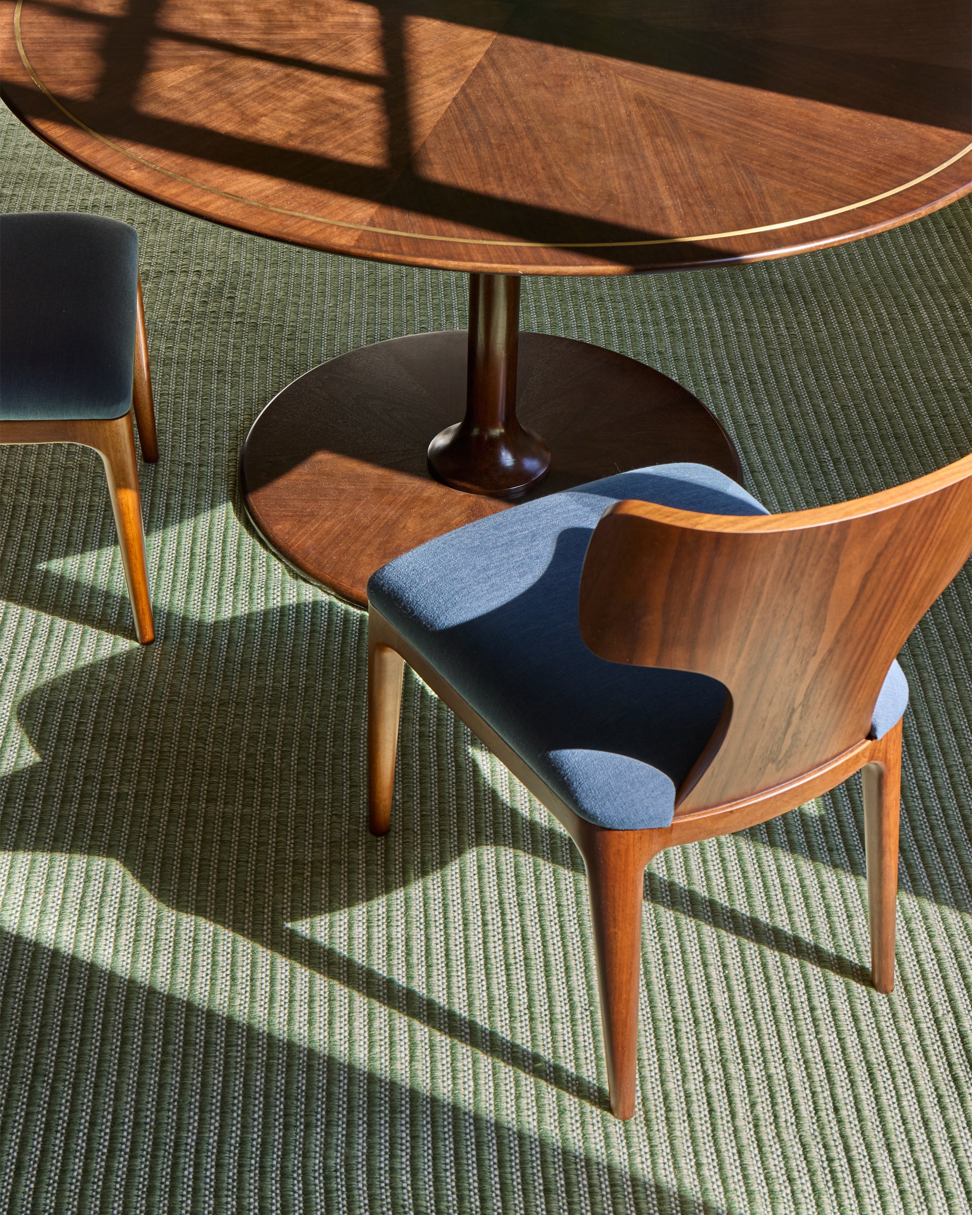 Wooden chairs with blue seats in a room with a wooden table and green carpet.