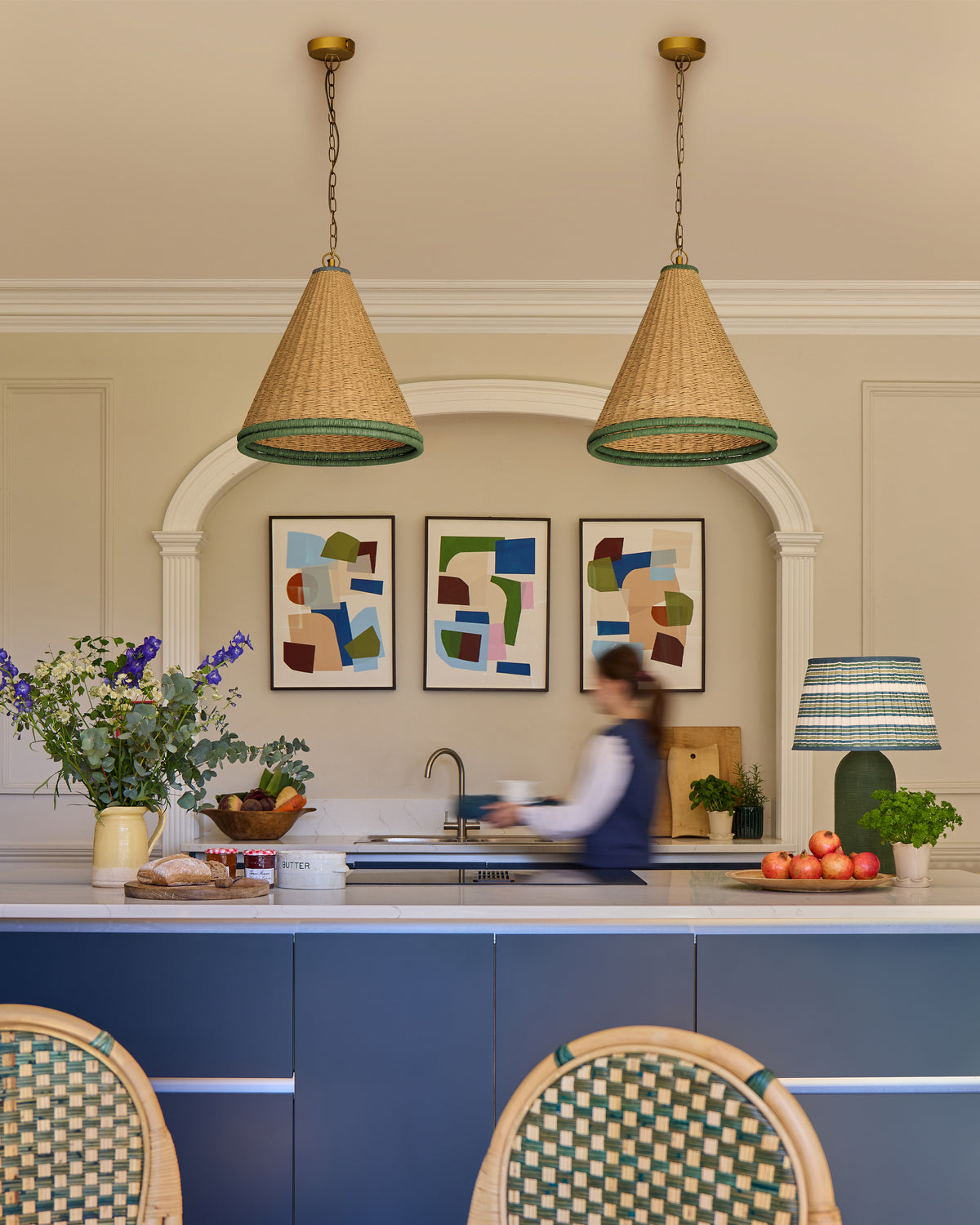 Kitchen interior with blue cabinetry, wicker pendant lights, and a person at the sink.