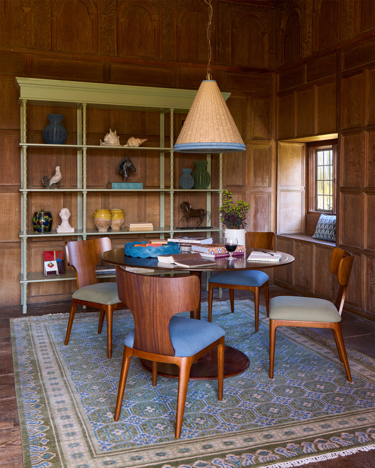 Dining room with wooden walls, round table, chairs, and a bookshelf.