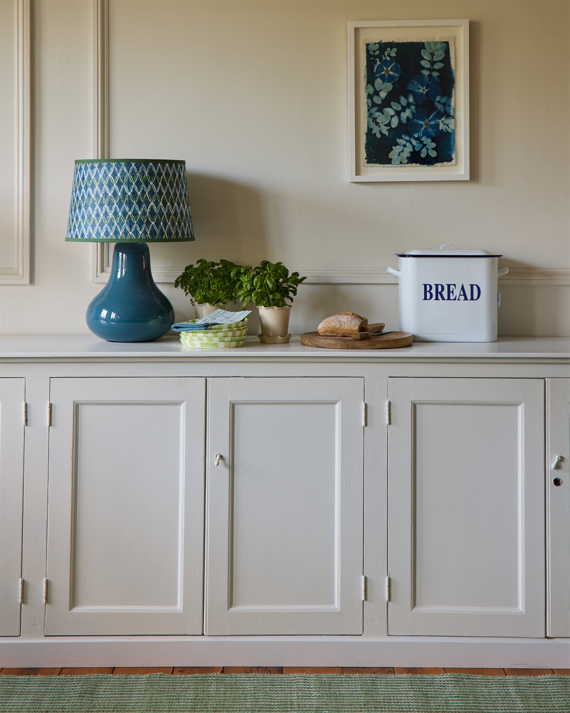Kitchen counter with a blue lamp, plants, and a bread bin in a room.