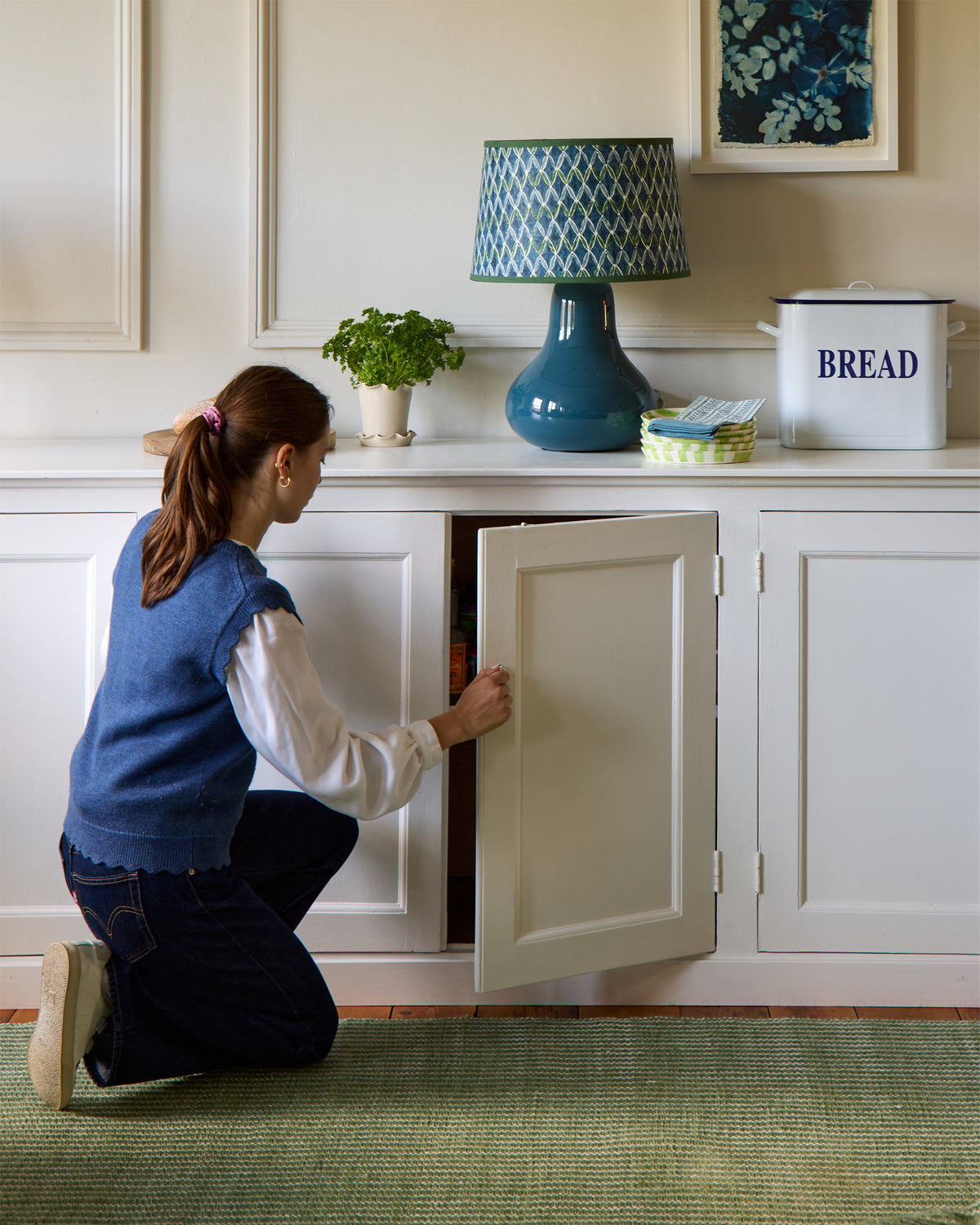 Person kneeling to look inside a cabinet in a kitchen.