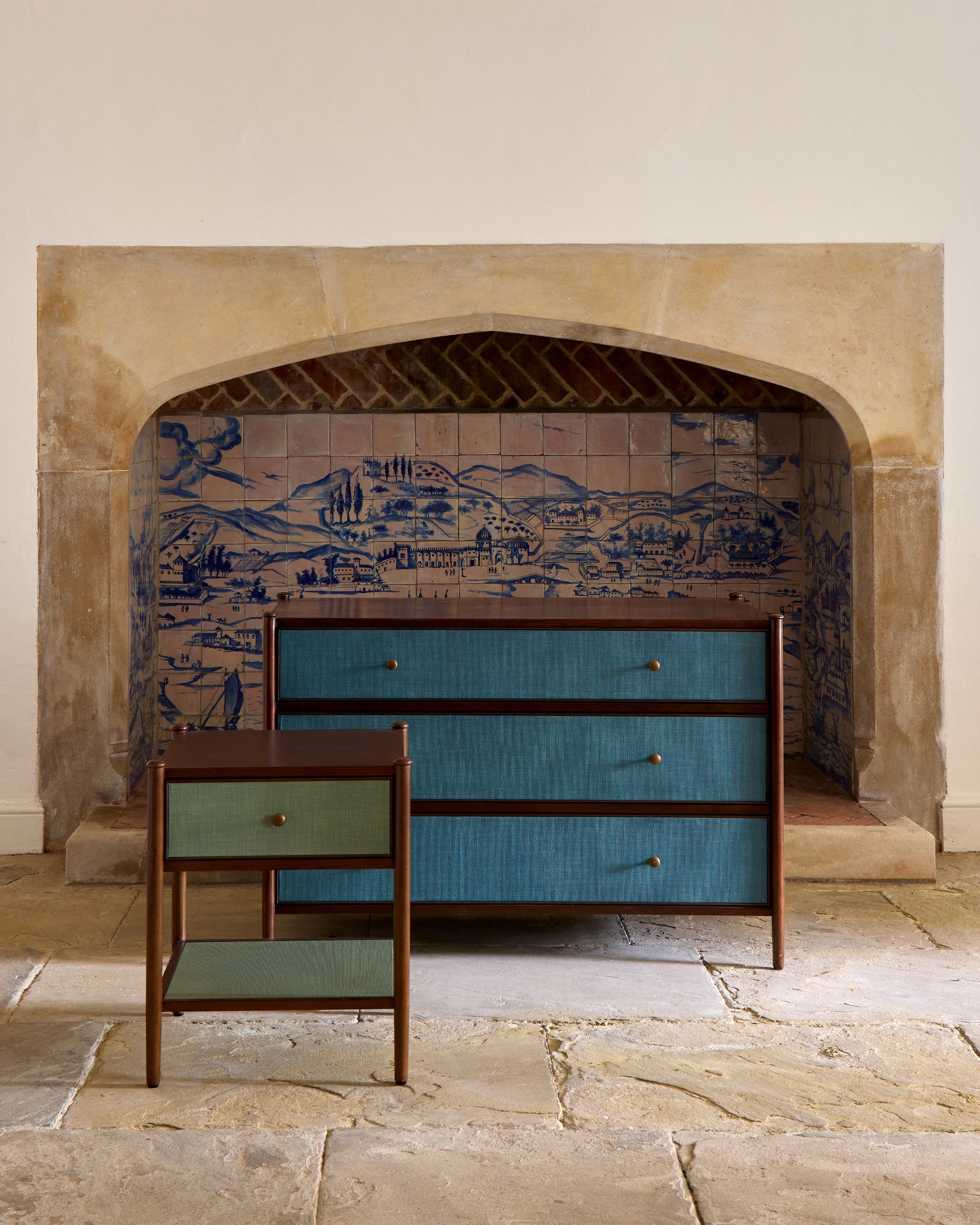 Blue dresser and side table in front of a decorative fireplace with tiled mural.