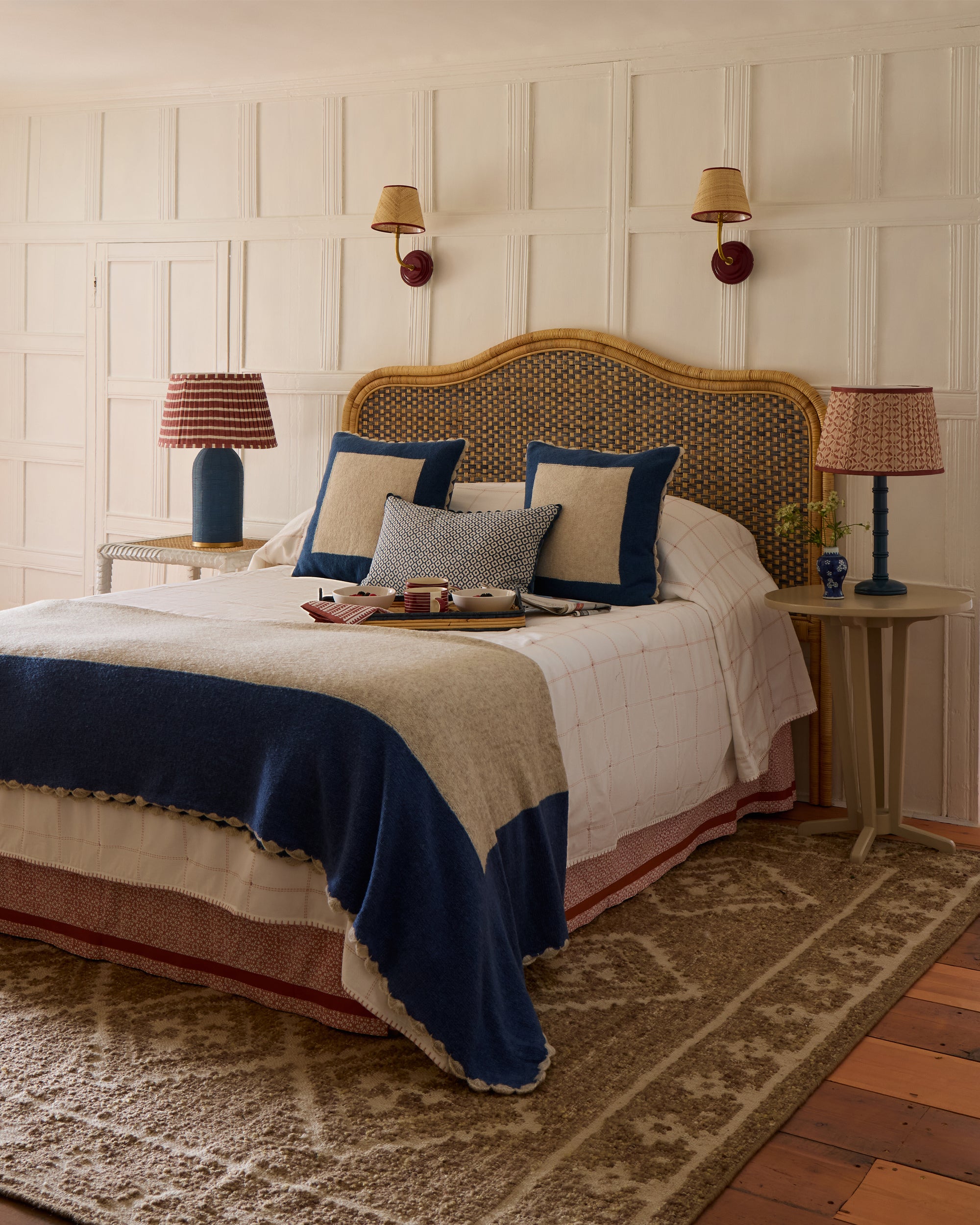 Decorative bedroom with a bed, cushions, and lamps against a panelled wall.