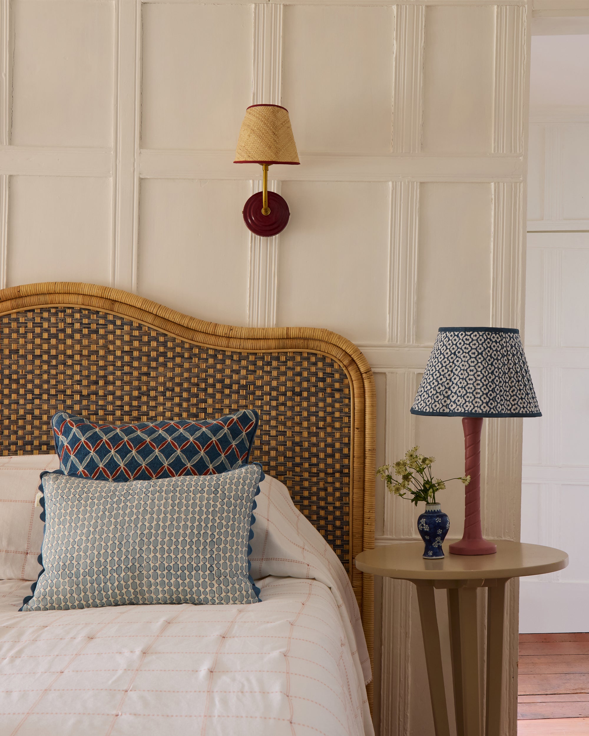 Bedroom with rattan headboard, cushions, and a side table with a lamp.