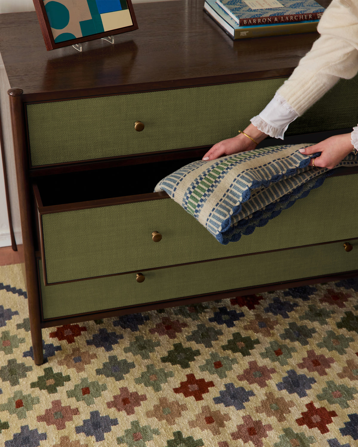 Person opening a green drawer with a patterned fabric inside, on a wooden dresser.
