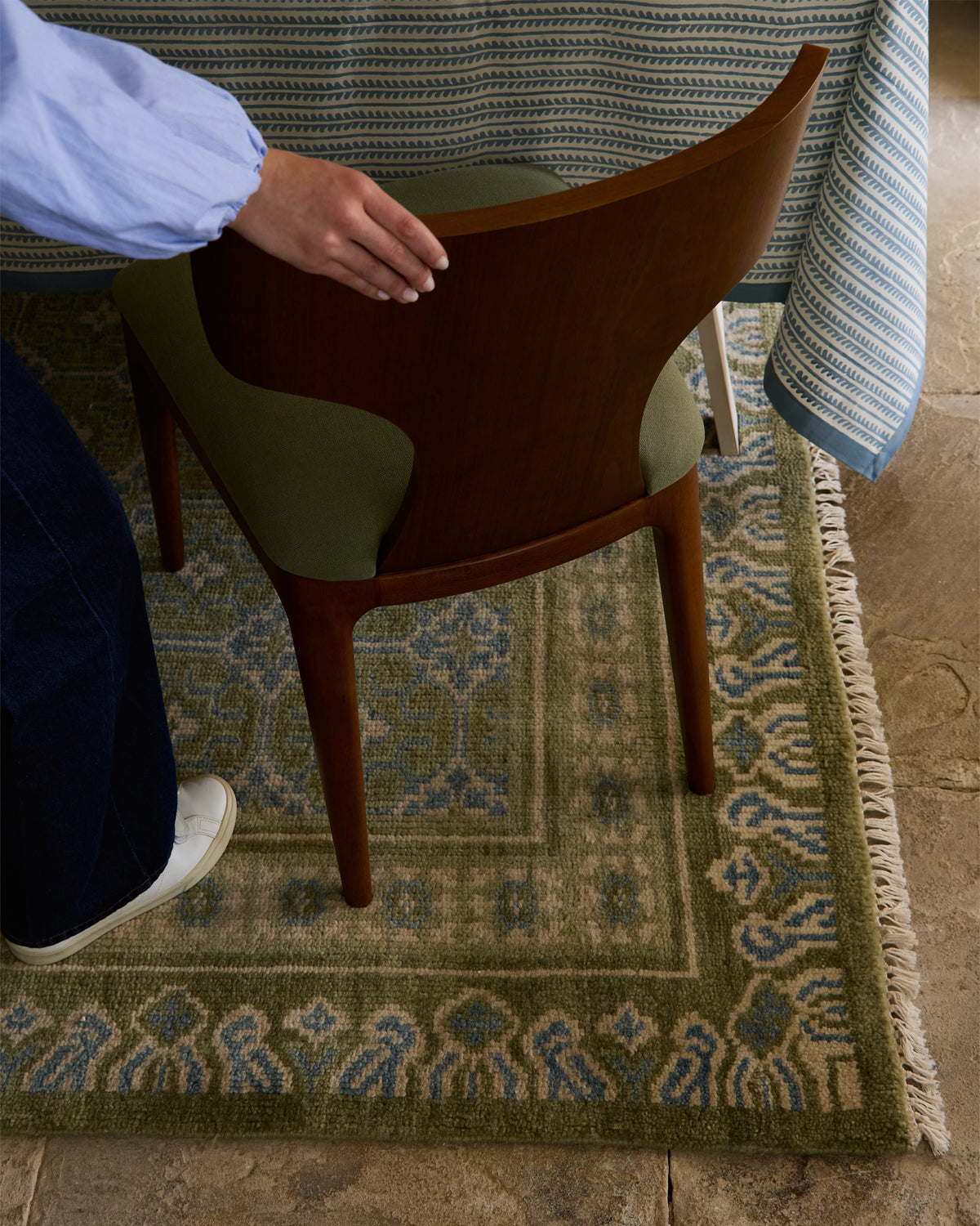 Person adjusting a chair on a patterned rug with a blue and white striped fabric in the background.