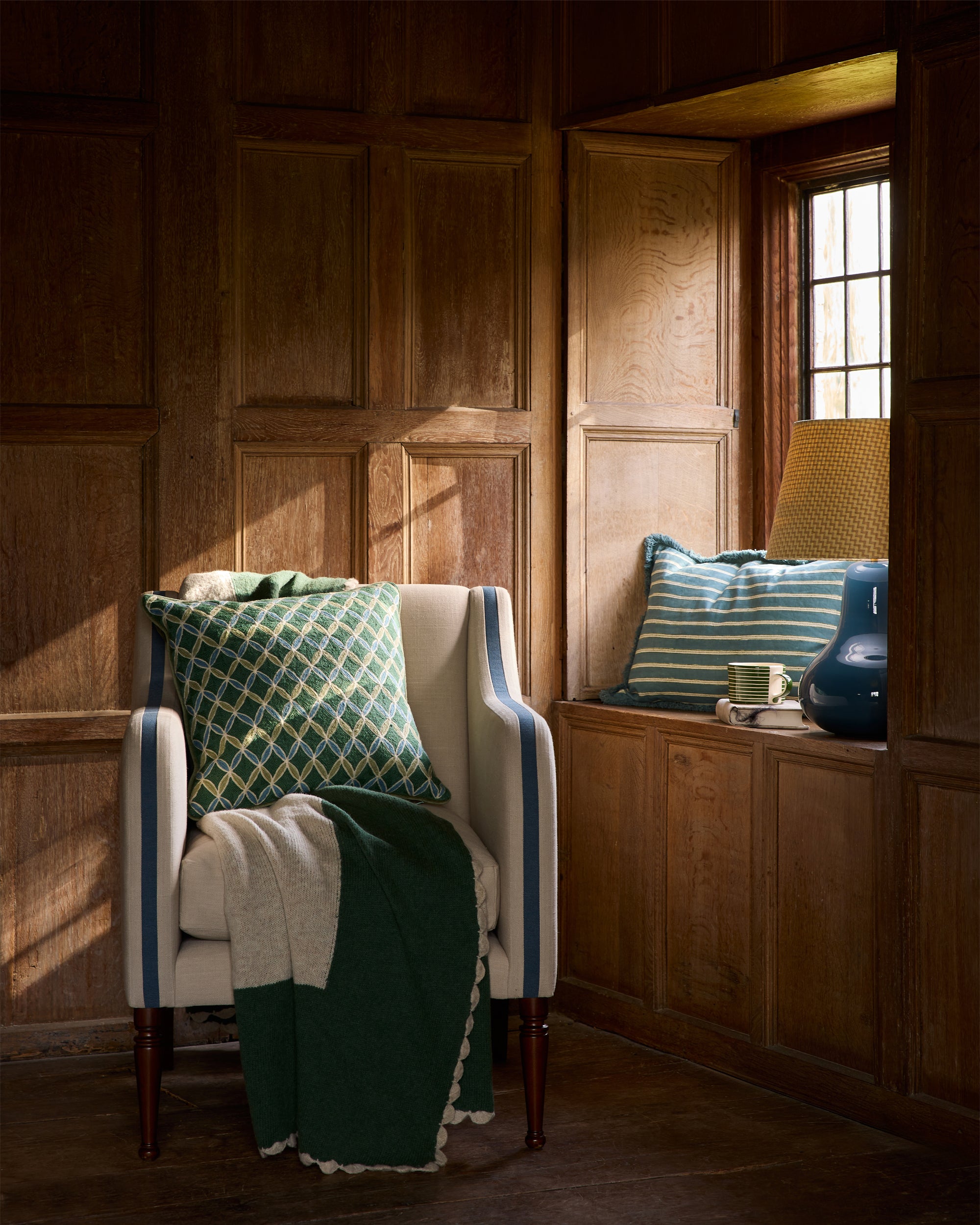 Chair with green and white patterned cushions in a room with wooden walls and a window.