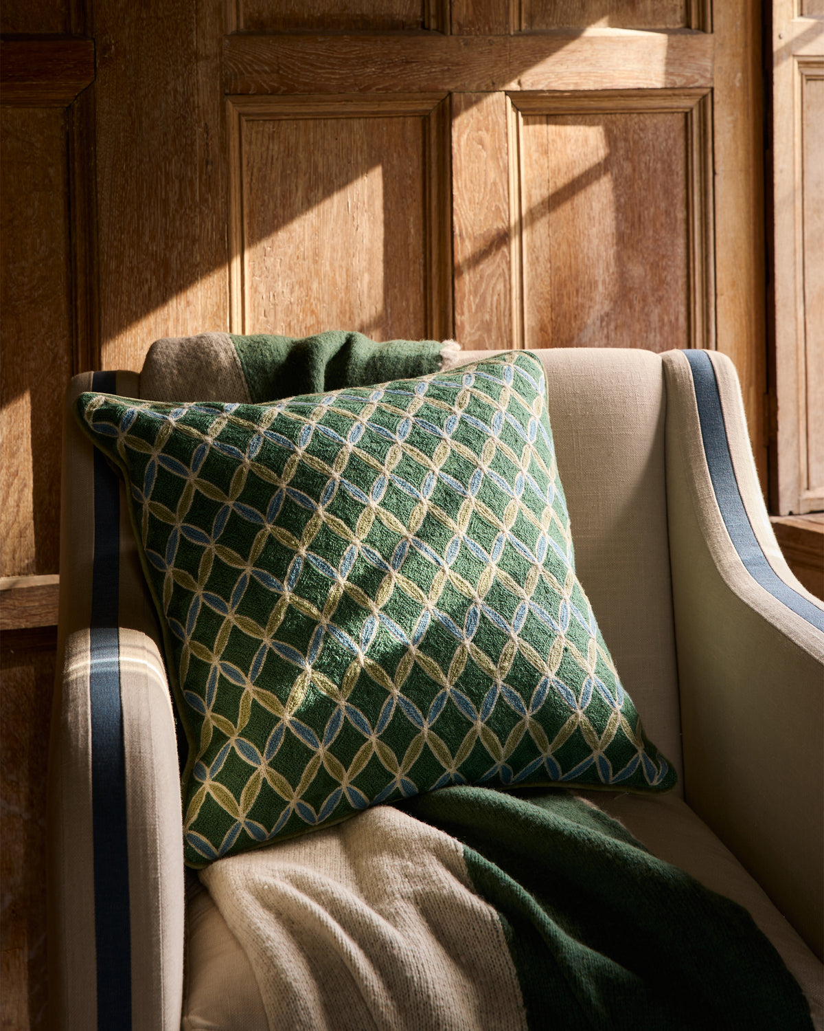 Green patterned cushion on a beige armchair against wooden paneling