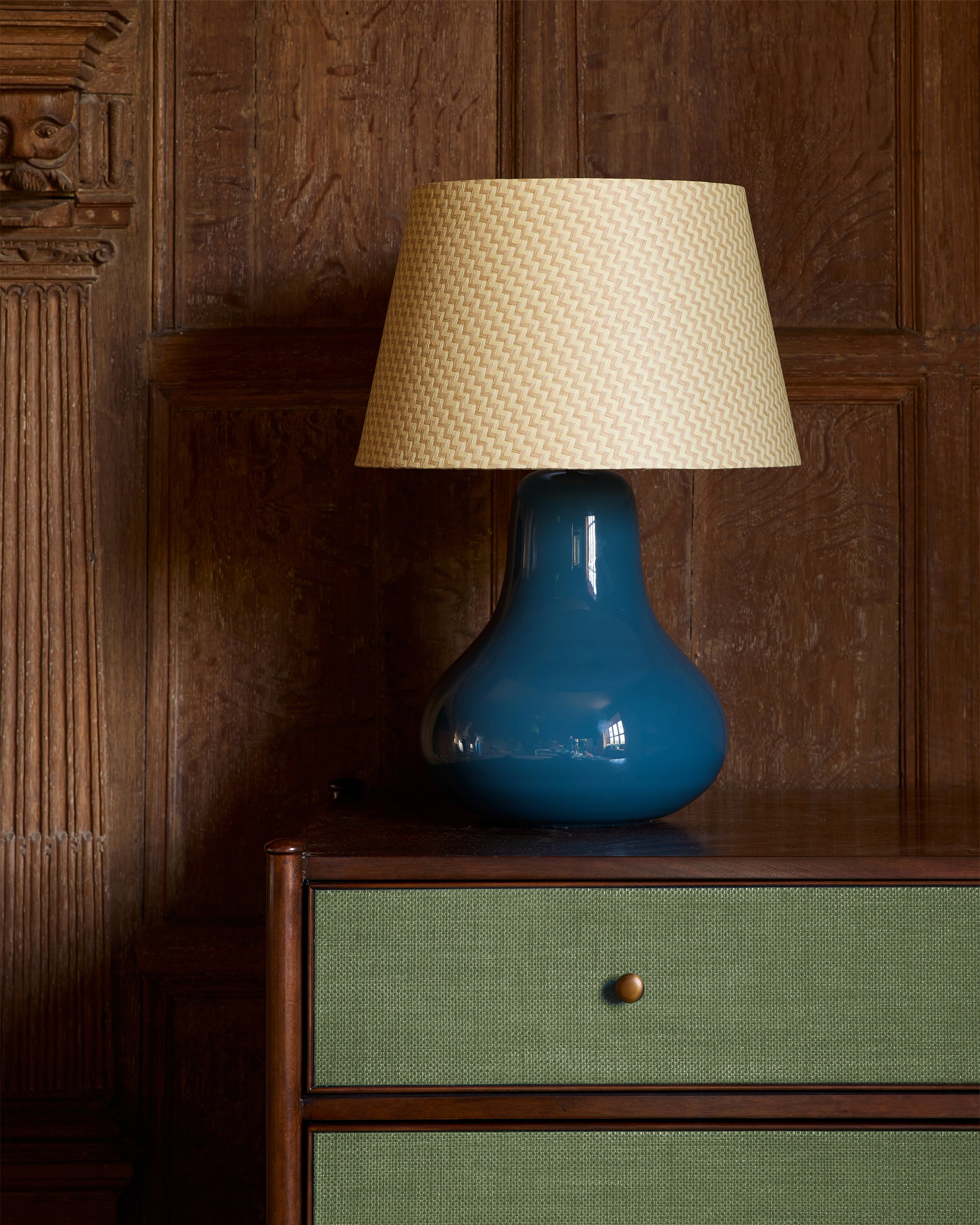 Blue lamp with a beige lampshade on a wooden cabinet against a wooden wall.