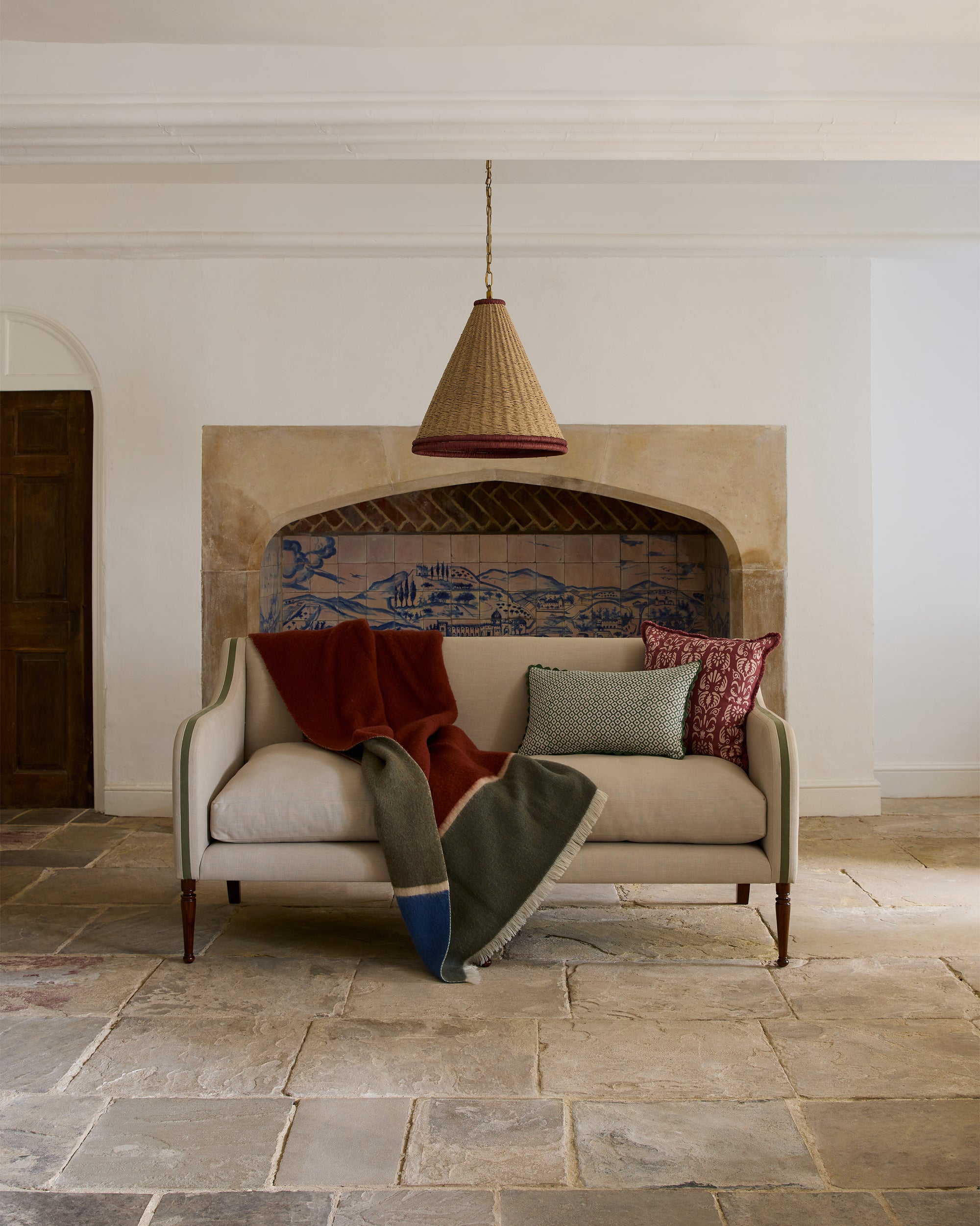Beige armchair with a blanket and cushions in a room with a stone fireplace.