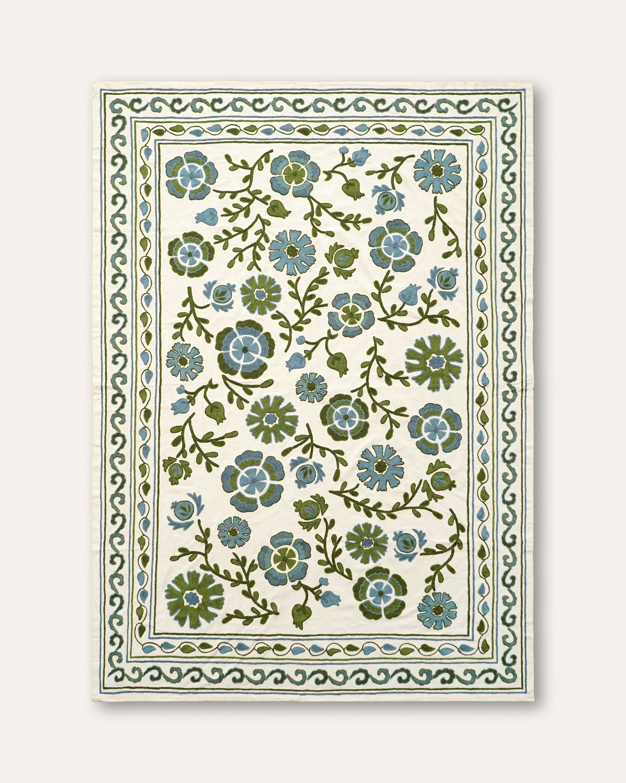 A rectangular suzani throw with a cream background, featuring a central floral pattern in sage green and dusty blue, surrounded by a decorative border.
