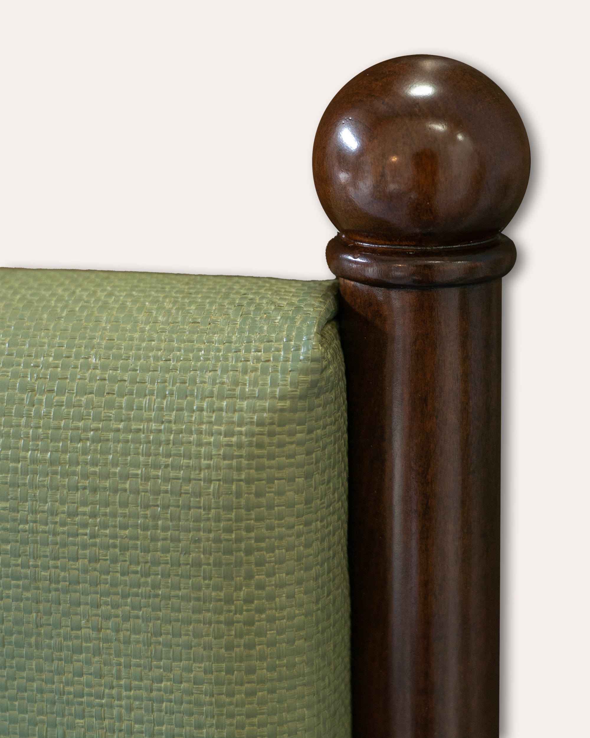 Close-up detail of a bed frame corner with a dark brown wooden post topped by a round finial next to an olive green upholstered headboard or side panel on a light neutral background.