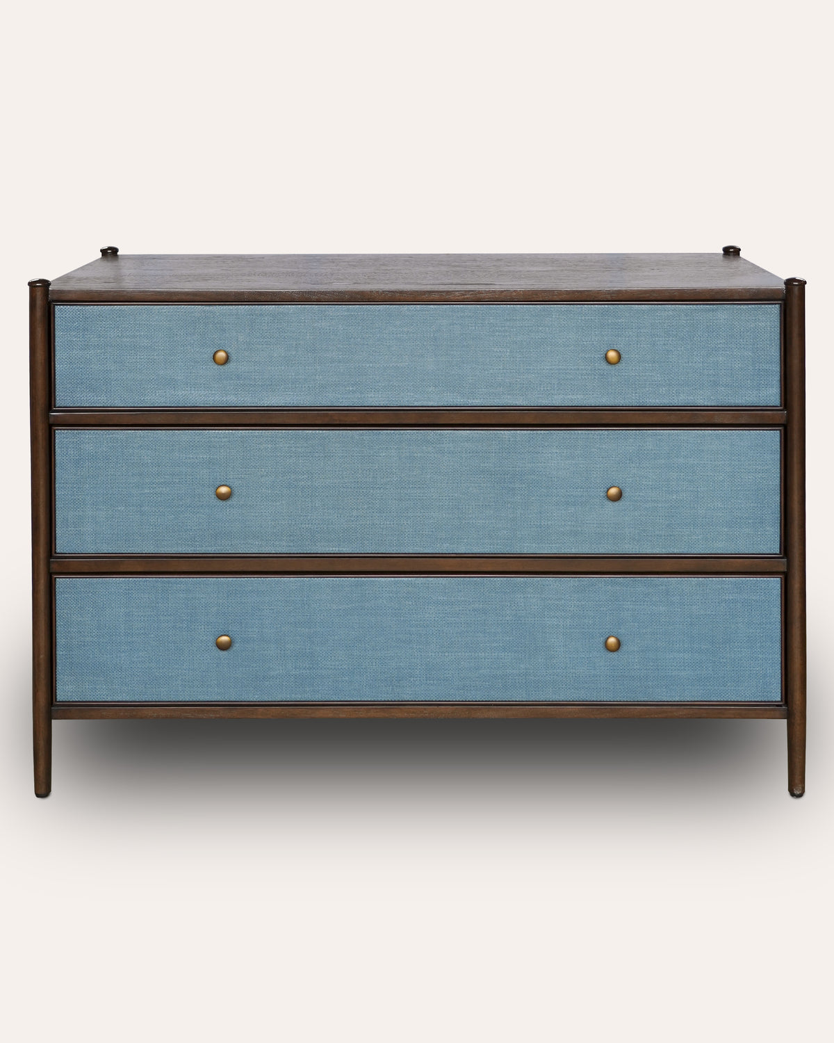 A three-drawer chest of drawers with a medium brown wood frame and light blue linen-textured drawer fronts, accented by small round brass knobs.