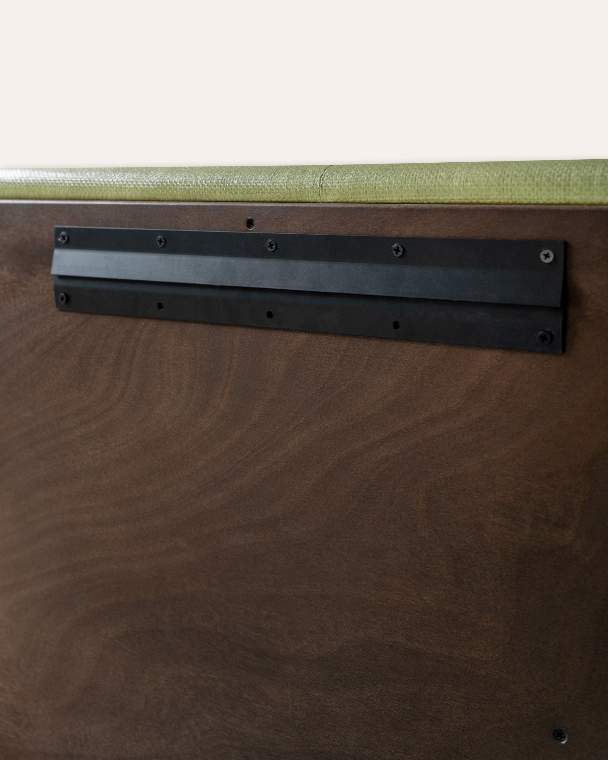 Close-up of a dark brown wood grain surface with a black metal mounting bracket attached near the top, below a light olive-green textured strip.