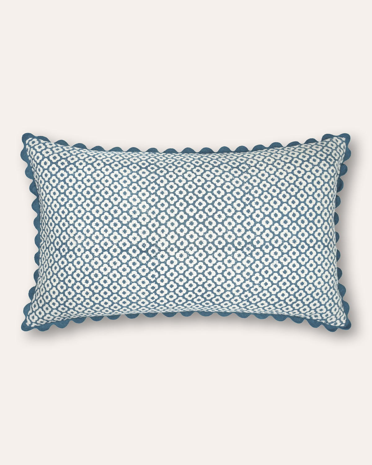 A rectangular cushion featuring a blue and white geometric diamond pattern and a scalloped blue border, shown against a solid off-white background.