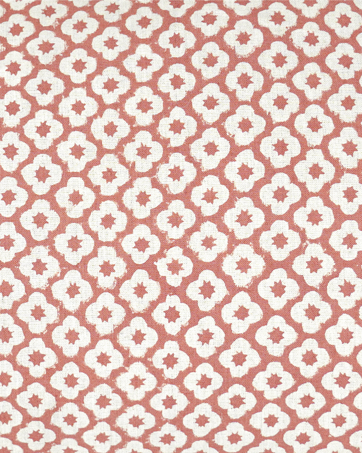 A close-up of a repeating fabric pattern featuring white quatrefoil-like motifs on a muted terracotta pink background.